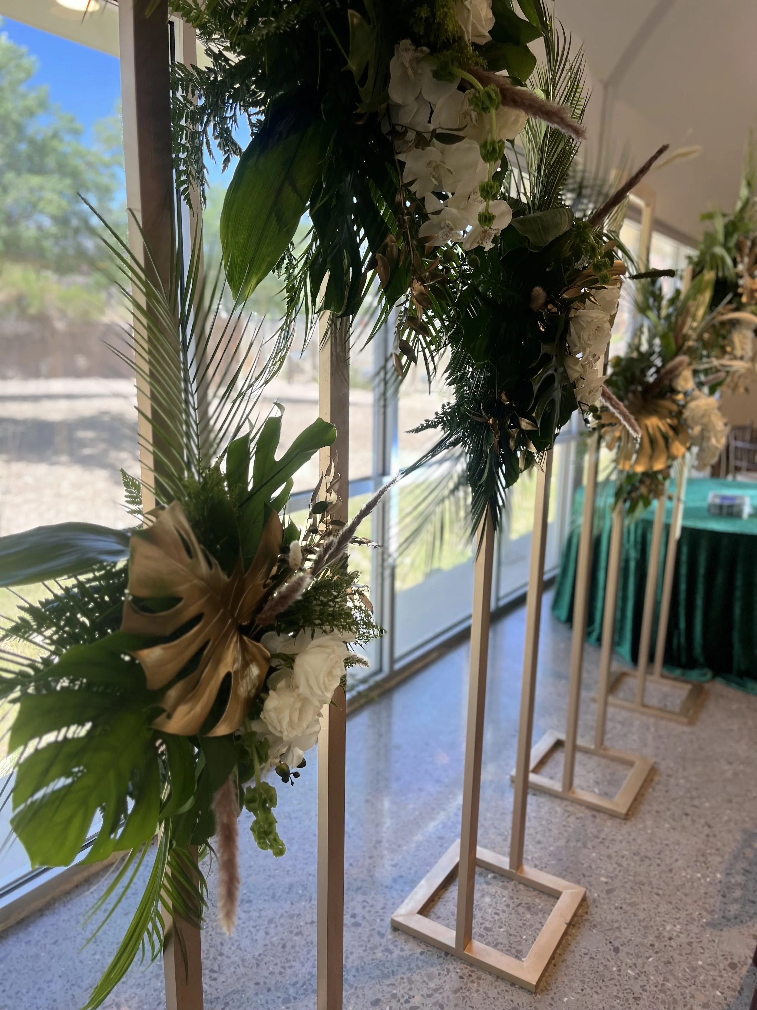 A floral arrangement on a wooden stand with tropical leaves and white flowers.