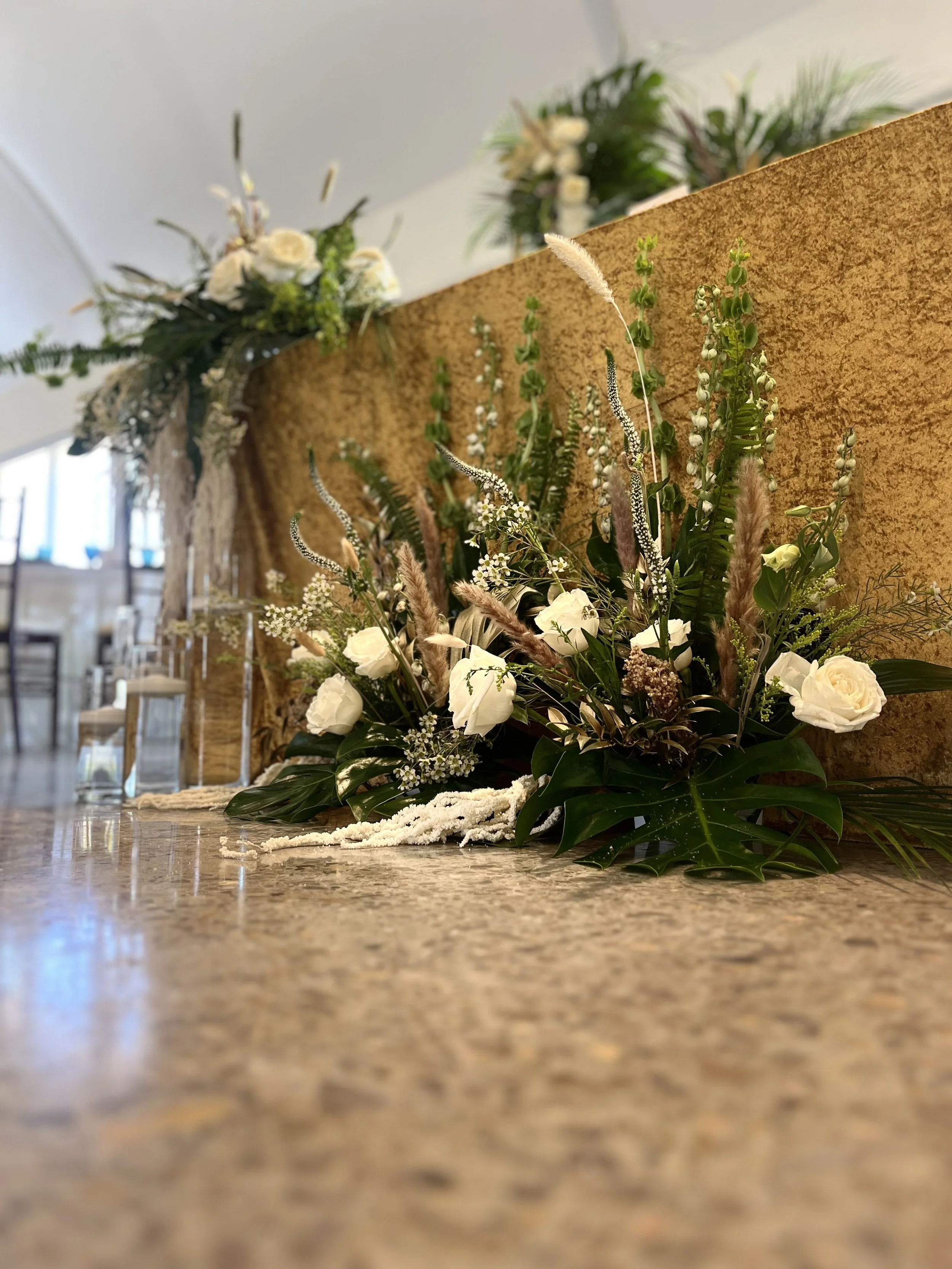 Floral arrangement with white roses, greenery, and decorative grasses .