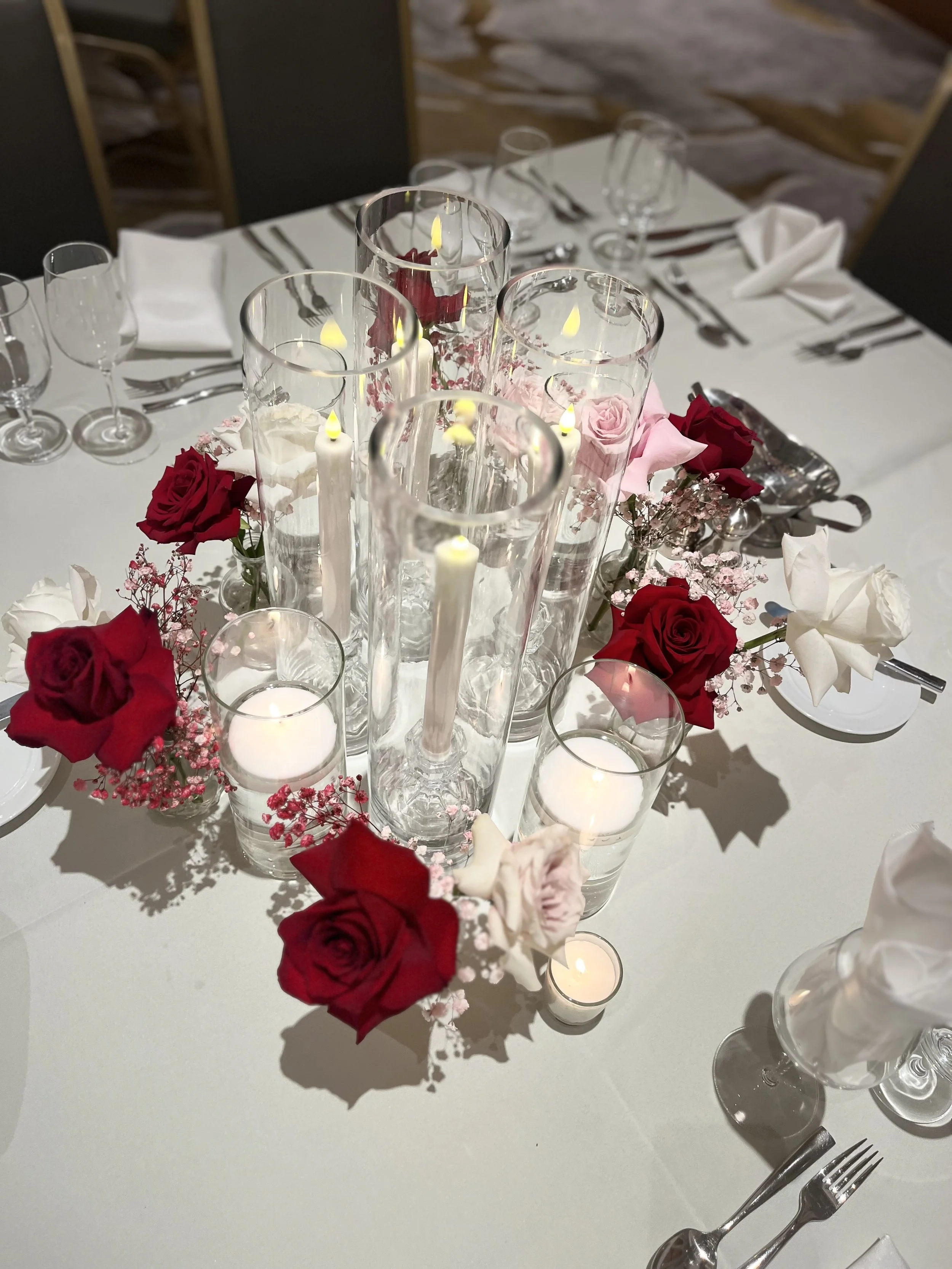 A round table decorated with red and white roses, pink baby's breath, candles in glass holders.