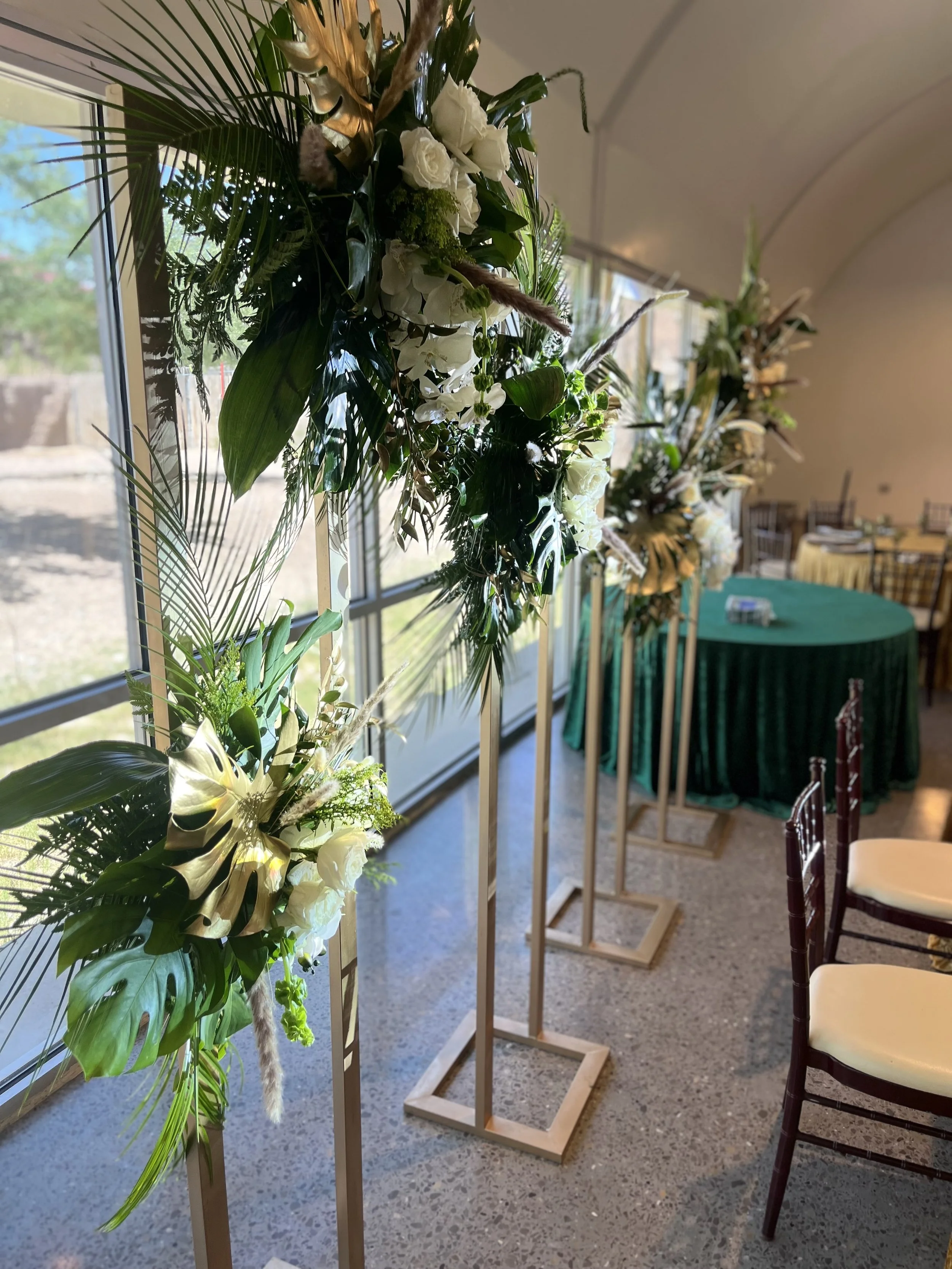 Tall floral arrangements with white flowers and green foliage on wooden stands.
