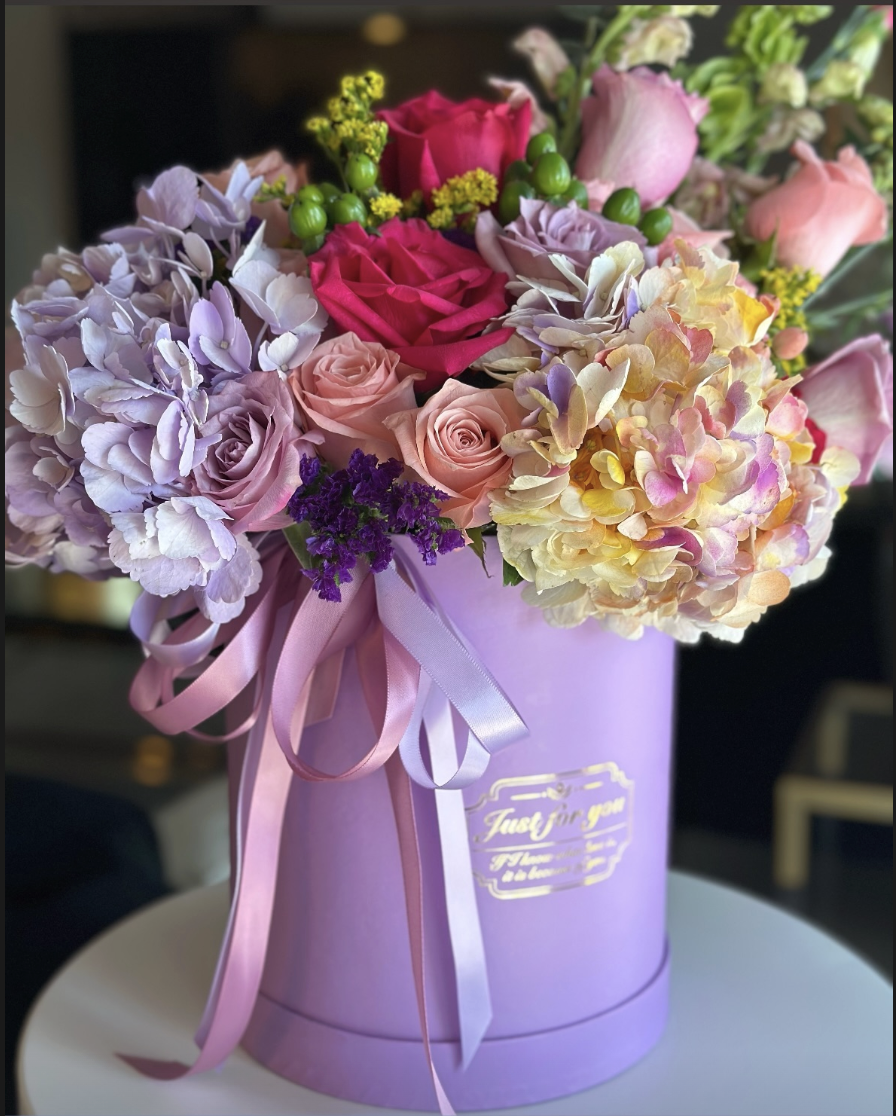 Arreglo floral con rosas, hortensias y otras flores en caja rosada con la leyenda 'Just for you'.