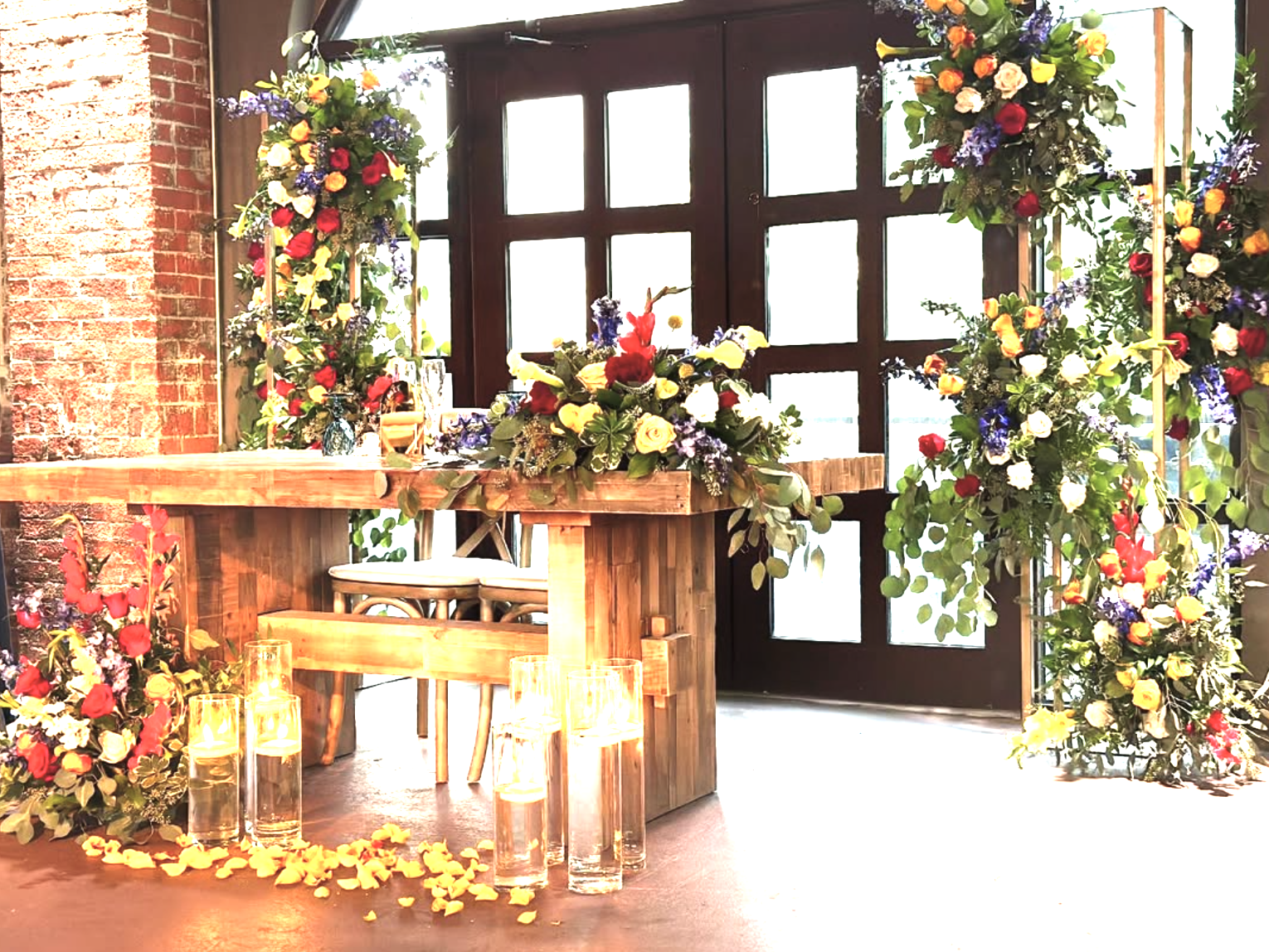 Decoración de boda con flores coloridas en un espacio con pared de ladrillos y puertas de madera