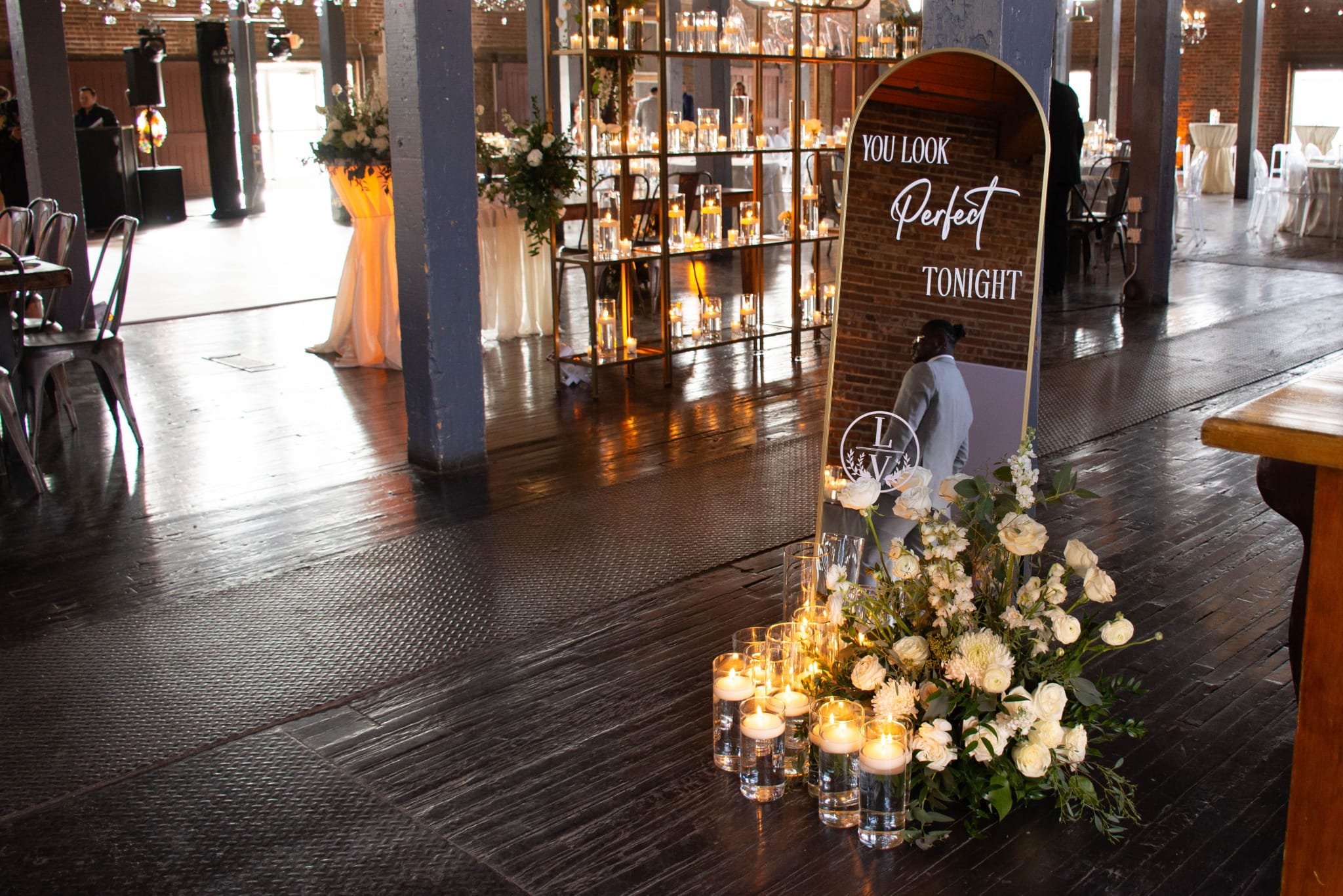 Wedding reception venue with floral arrangements, candles, and a mirror sign.