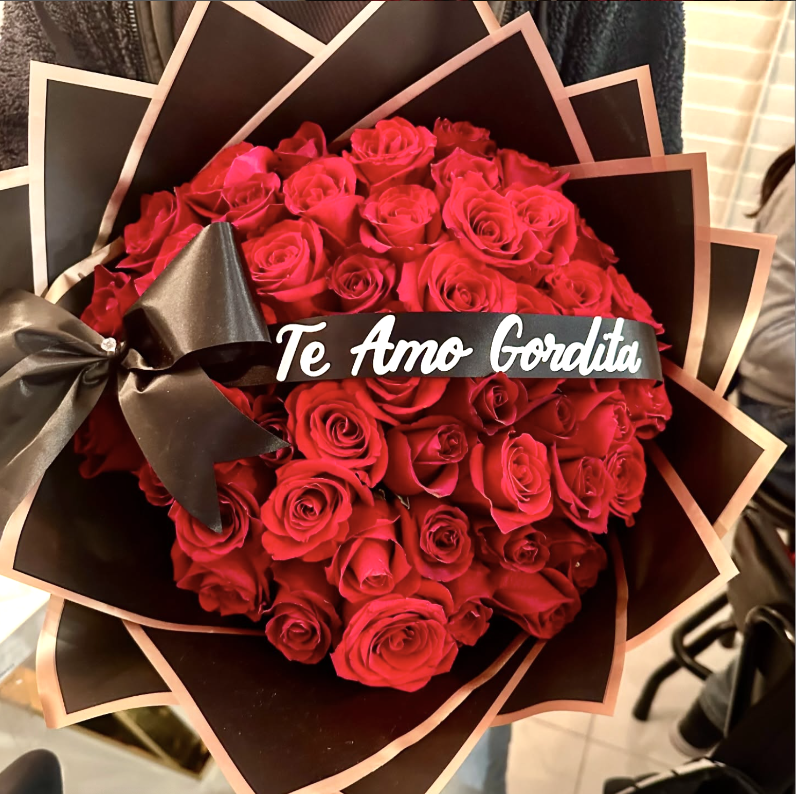 Ramo de rosas rojas con una cinta negra y una tarjeta que dice 'Te Amo Gordita' en letras blancas.
