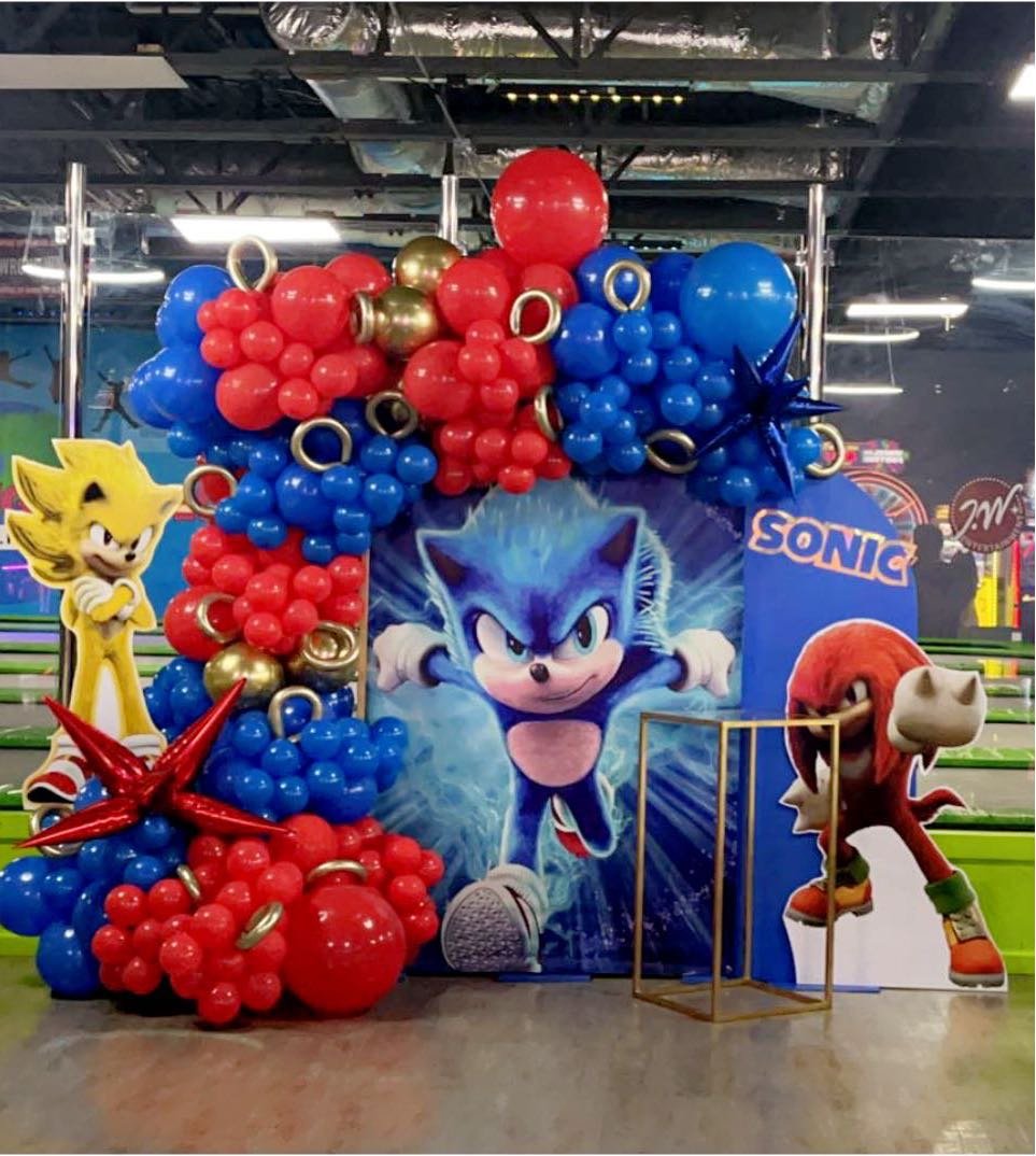 Colorful Sonic the Hedgehog-themed balloon decoration with a large Sonic poster in the center, surrounded by red, blue, and gold balloons, and cardboard cutouts of Sonic, Tails, and Knuckles.