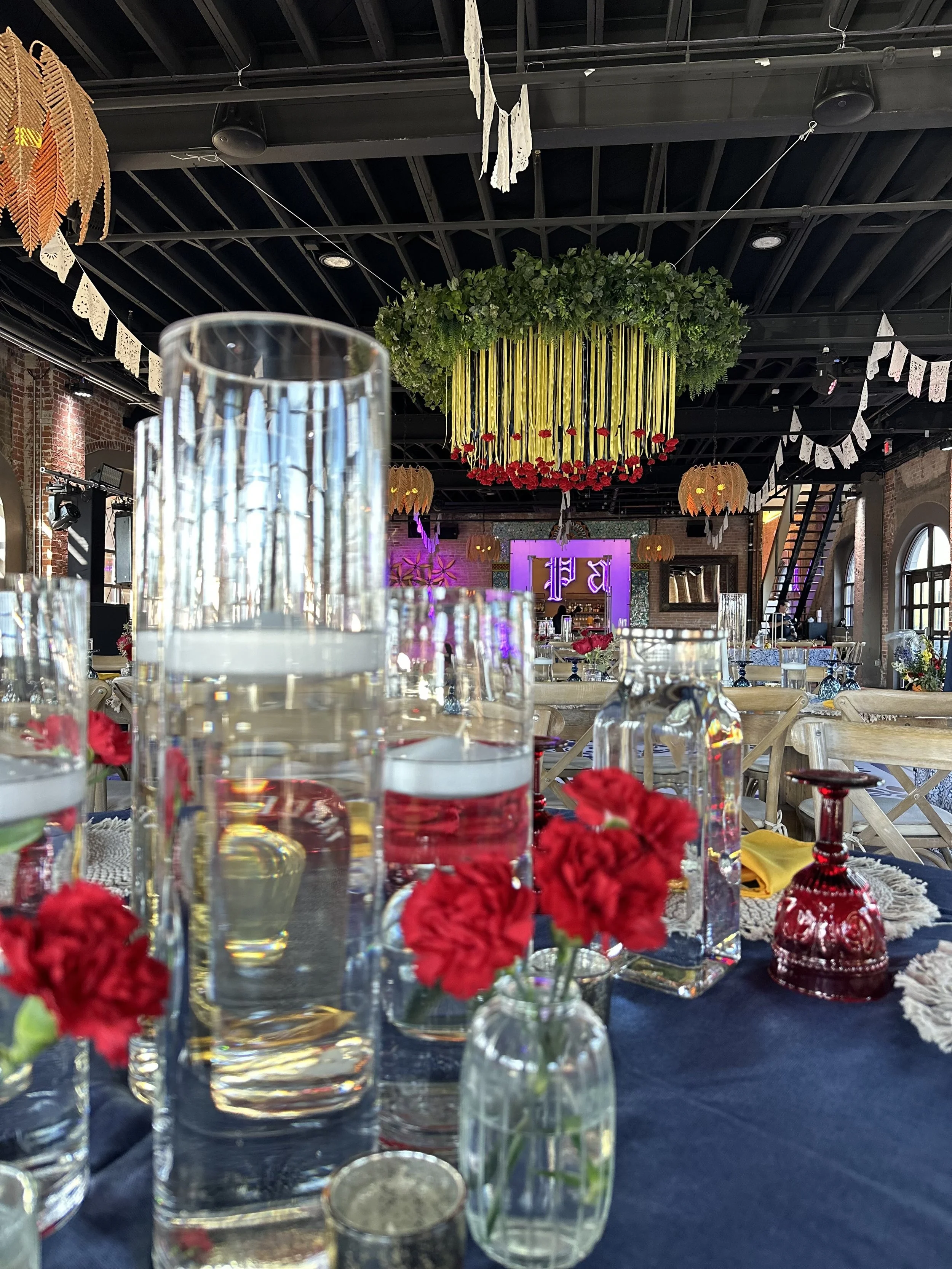 Decorated event space with tall glass vases and red carnations on tables.