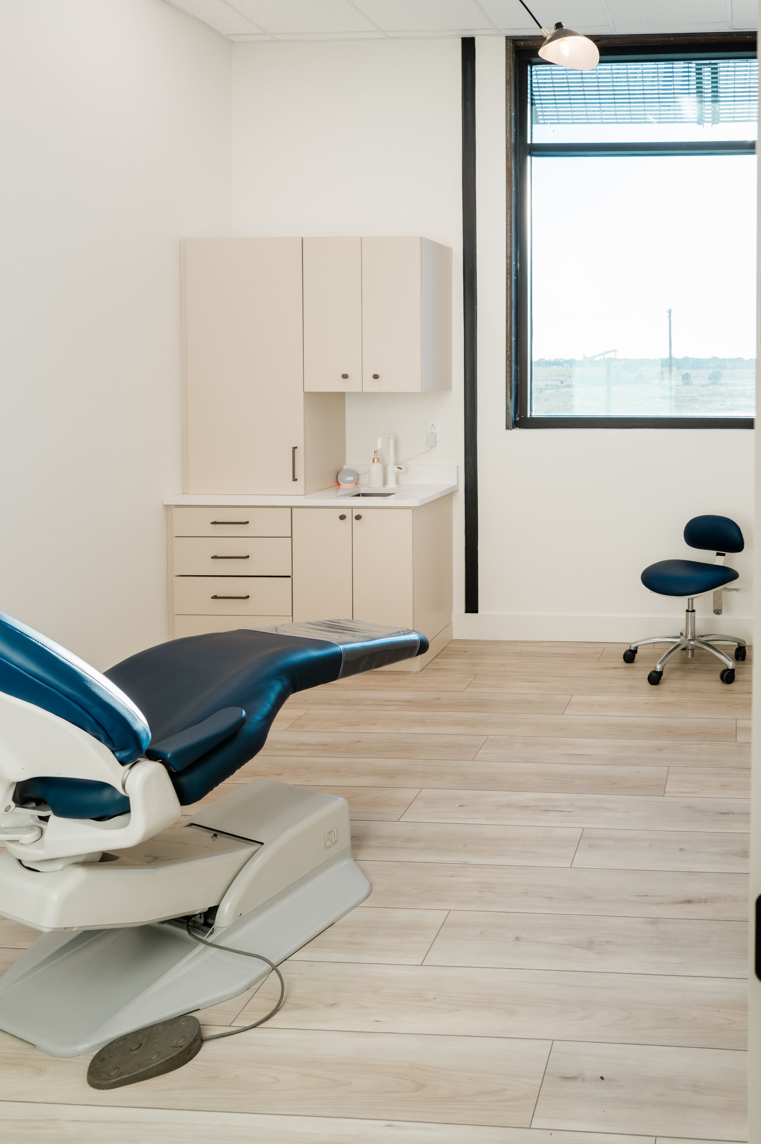 Natural Skin Health Consultation Room - color pallete is neutral tones with a navy blue reclined chair for the patient. There is a lovely large window to let in natural light.