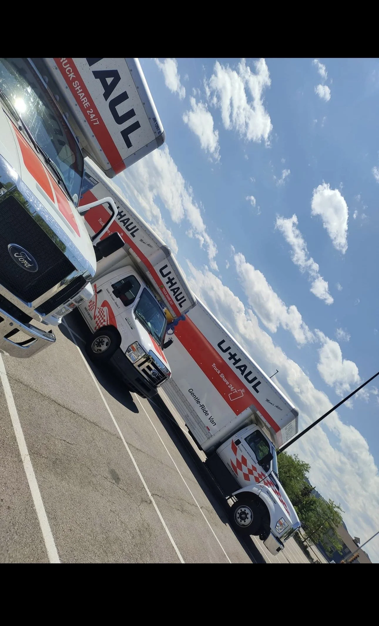U-Haul trucks and a Ford van parked in a lot under a blue sky with white clouds.