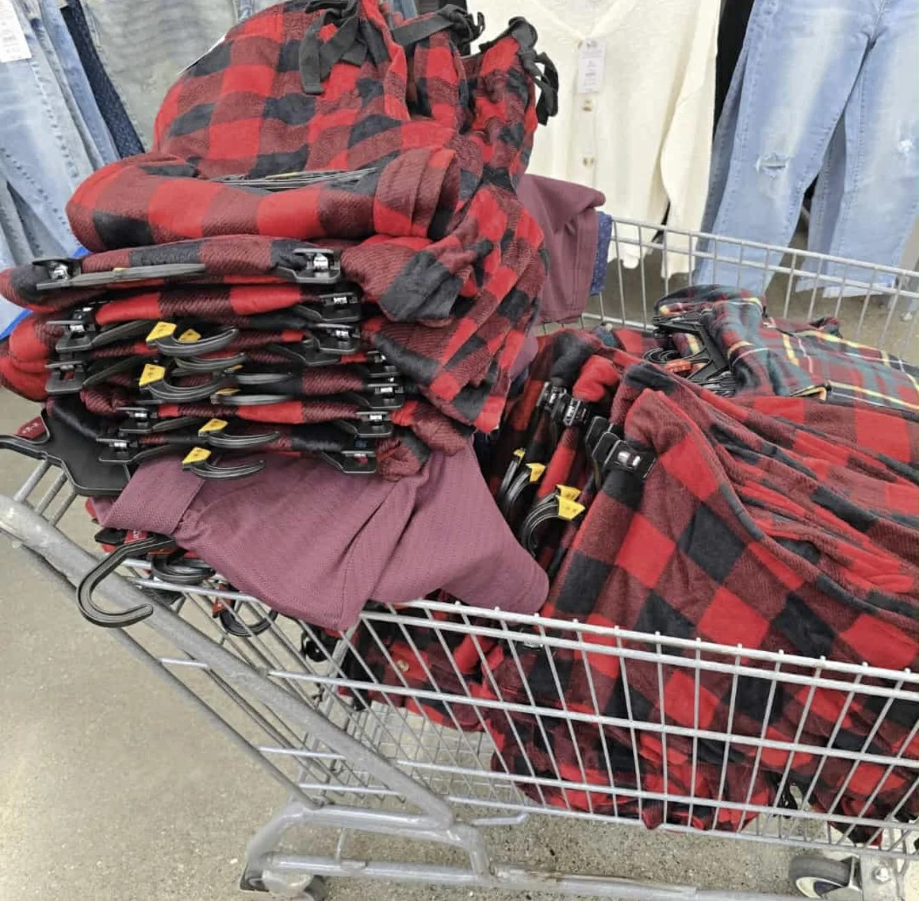 Shopping cart filled with red and black plaid shirts, some maroon pants, and black accessories in a clothing store.