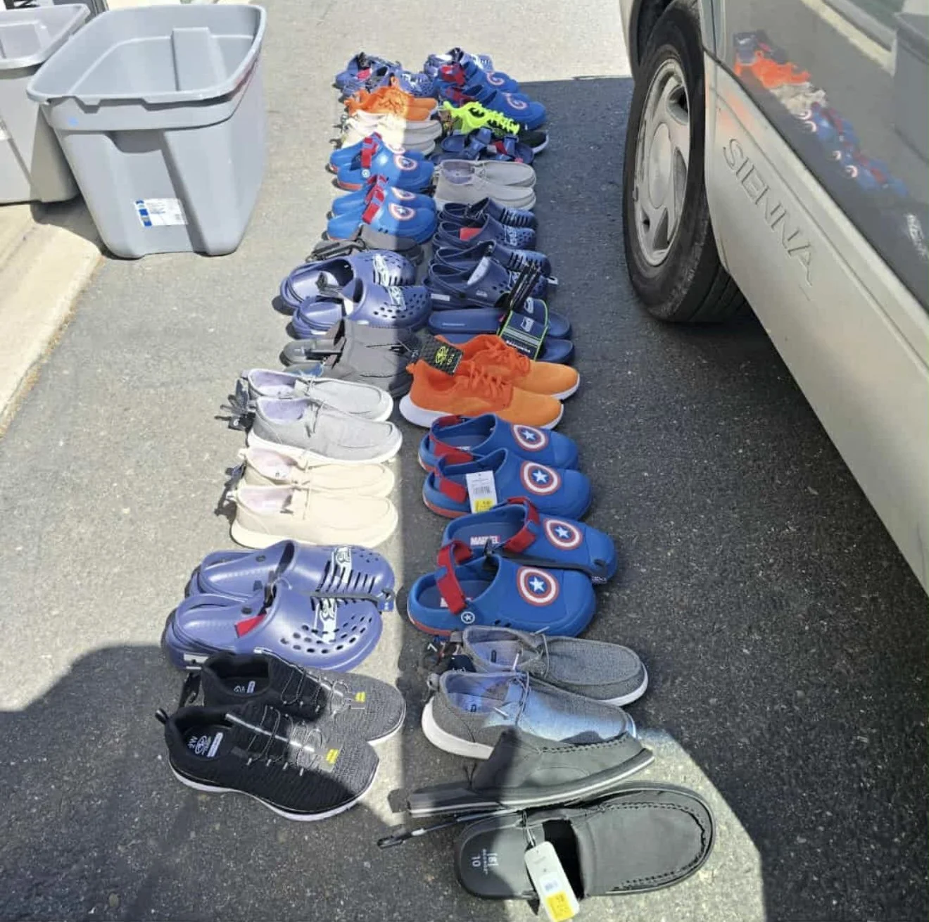 Collection of children's shoes, including sneakers and sandals, arranged on the ground outside a vehicle for sale.