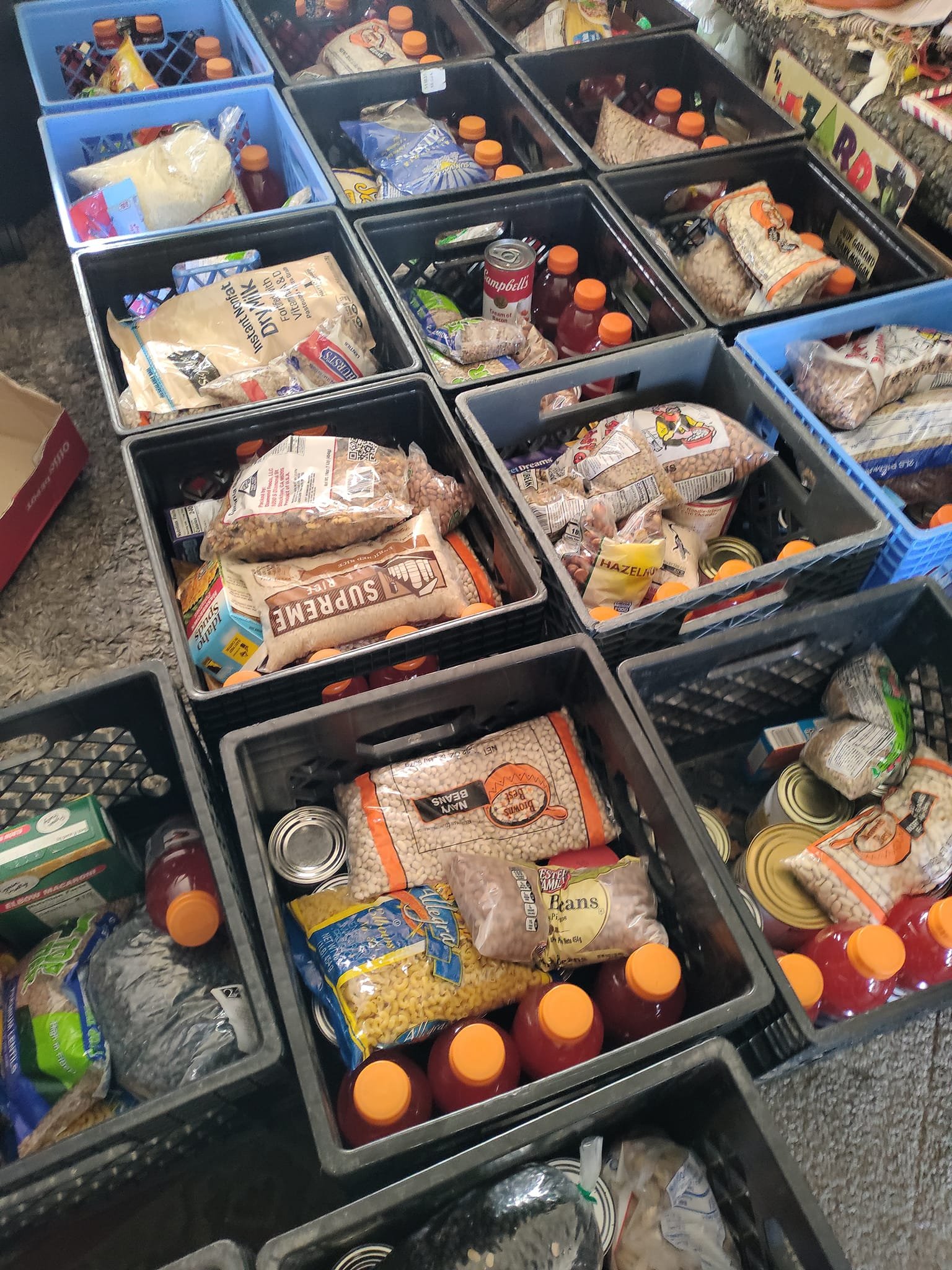 Multiple black and blue plastic bins filled with food items and bottled drinks in a grocery store.