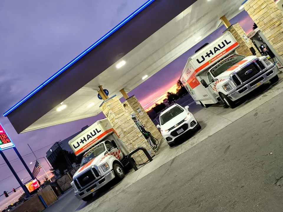 U-Haul trucks and a white car parked at a gas station during sunset.