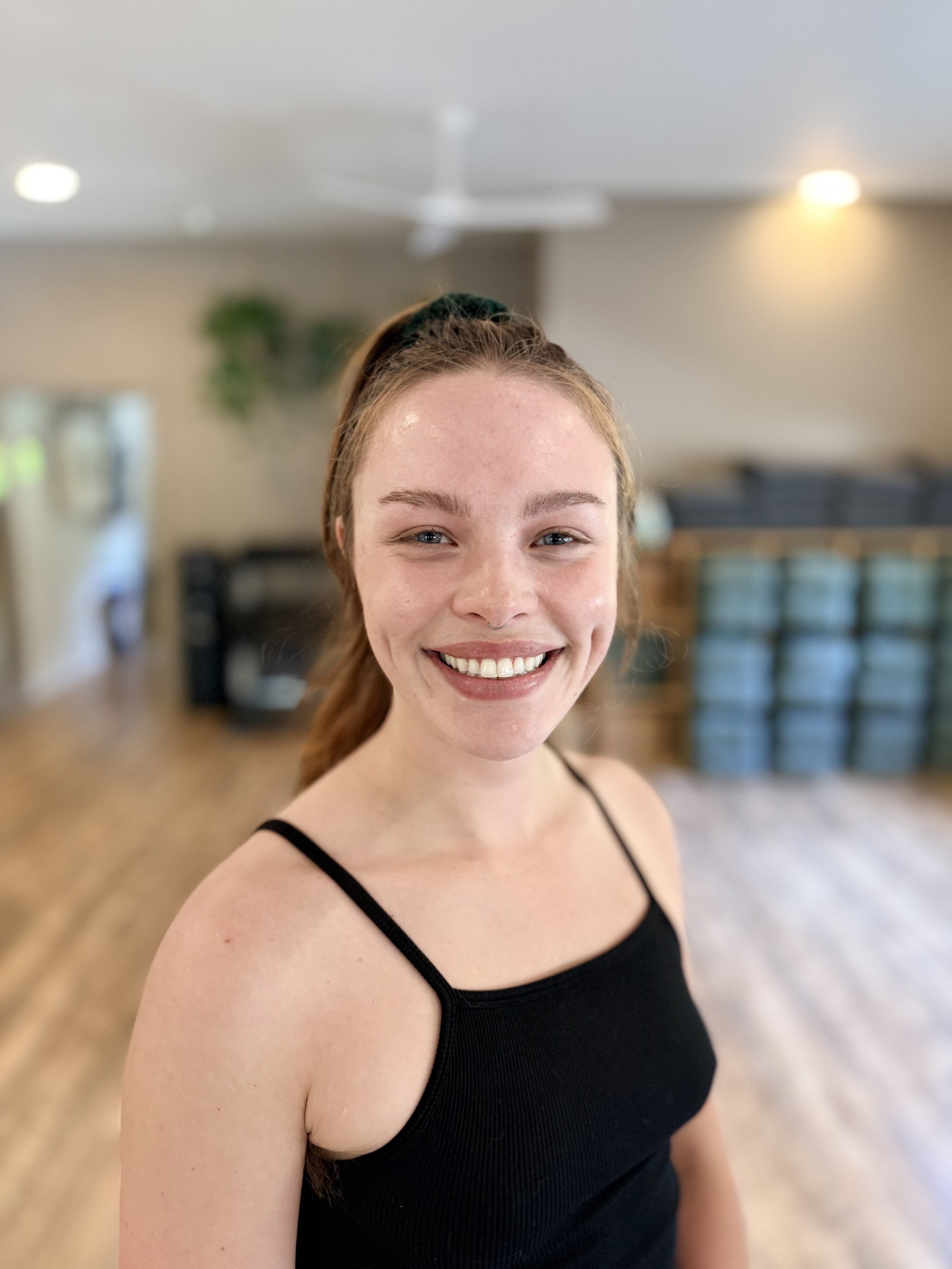 a blonde woman with a big smile and a ponytail inside a yoga studio