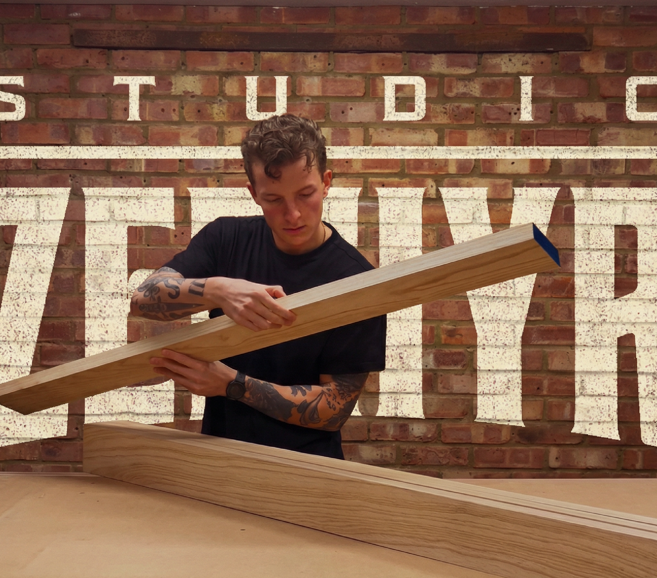 A tattooed man is checking the quality of some solid timber boards in a joinery workshop
