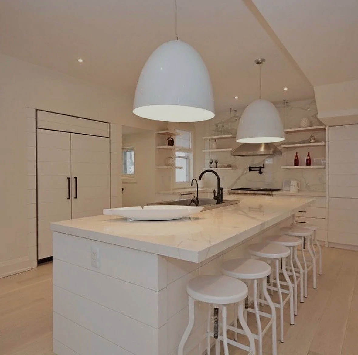 Modern kitchen with a white marble island, black faucets, hanging white pendant lighting, open shelving, and minimalist decor.