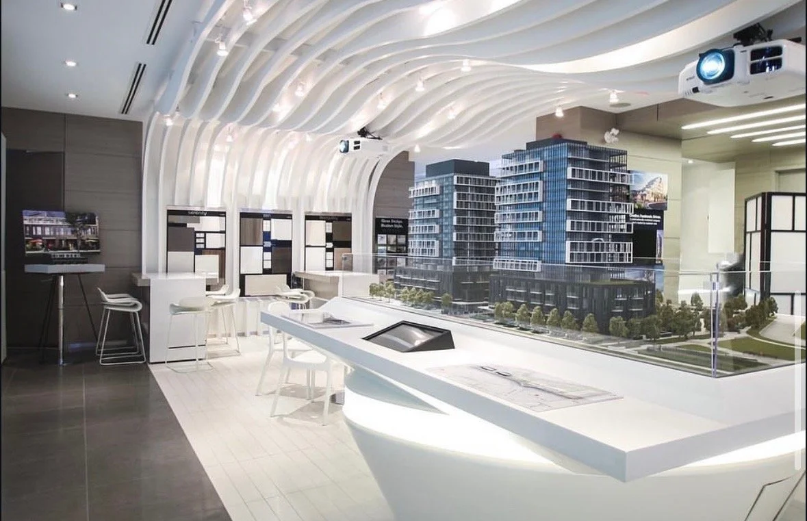 Architectural model display of modern multi-story buildings in a showroom or presentation space with a curved white ceiling.