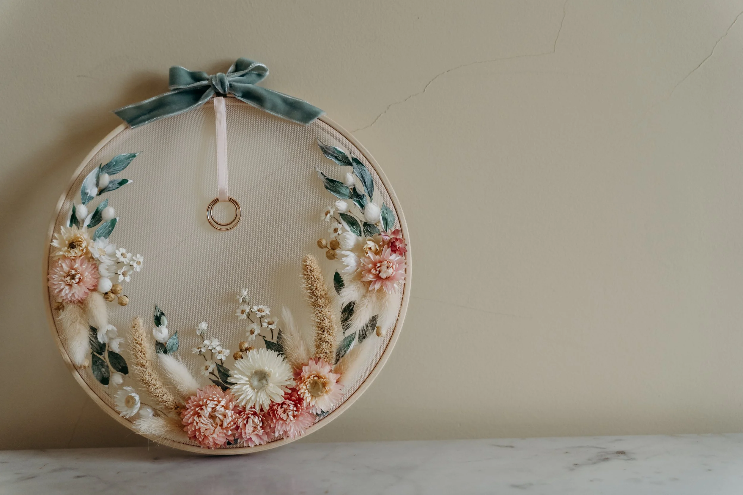 Decorative floral hoop with a gray ribbon bow hanging on a beige wall.