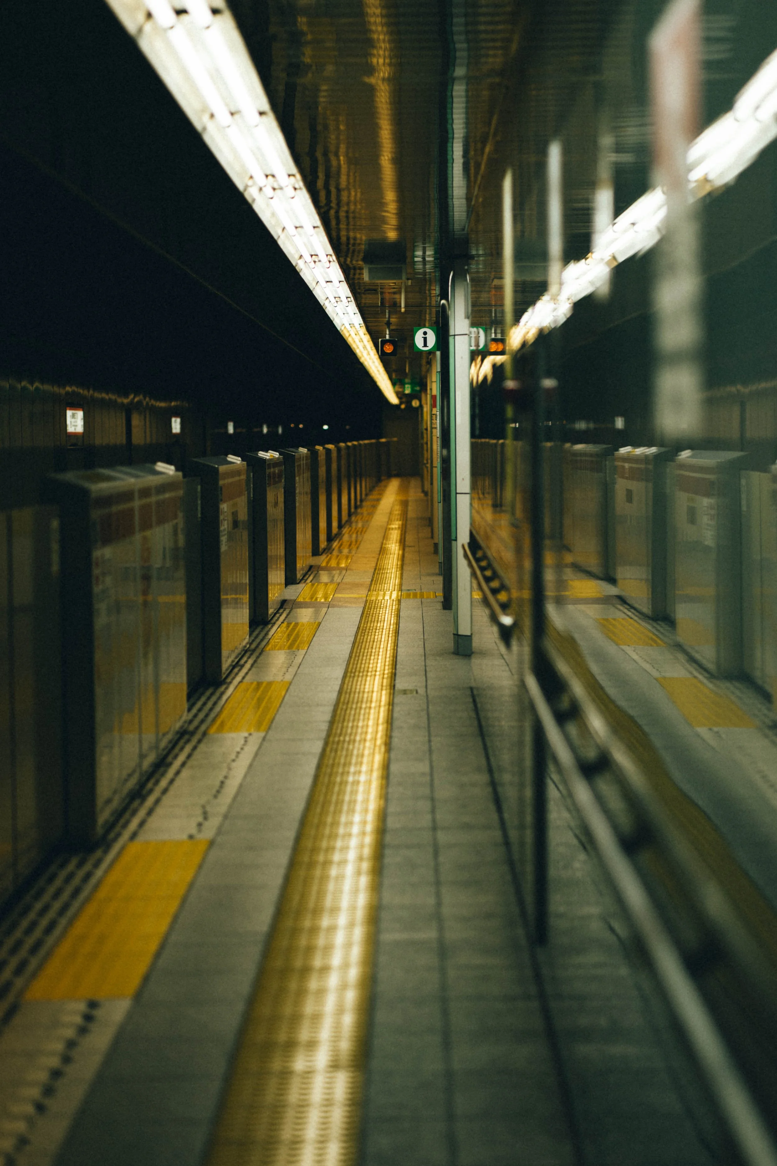 Empty subway platform with a yellow tactile paving strip and glass reflecting the platform's edge lights.