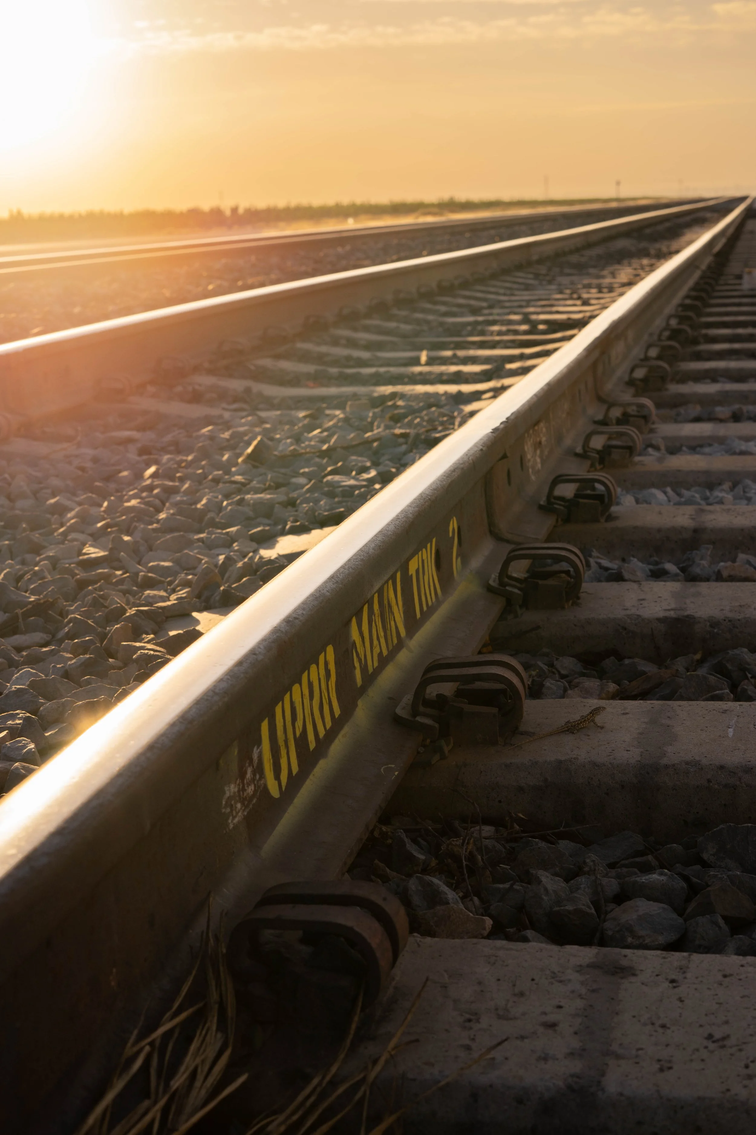 Close-up view of railroad track at sunset with a bright sun on the left side and a yellow warning sign on the track that reads 'Caution the'.