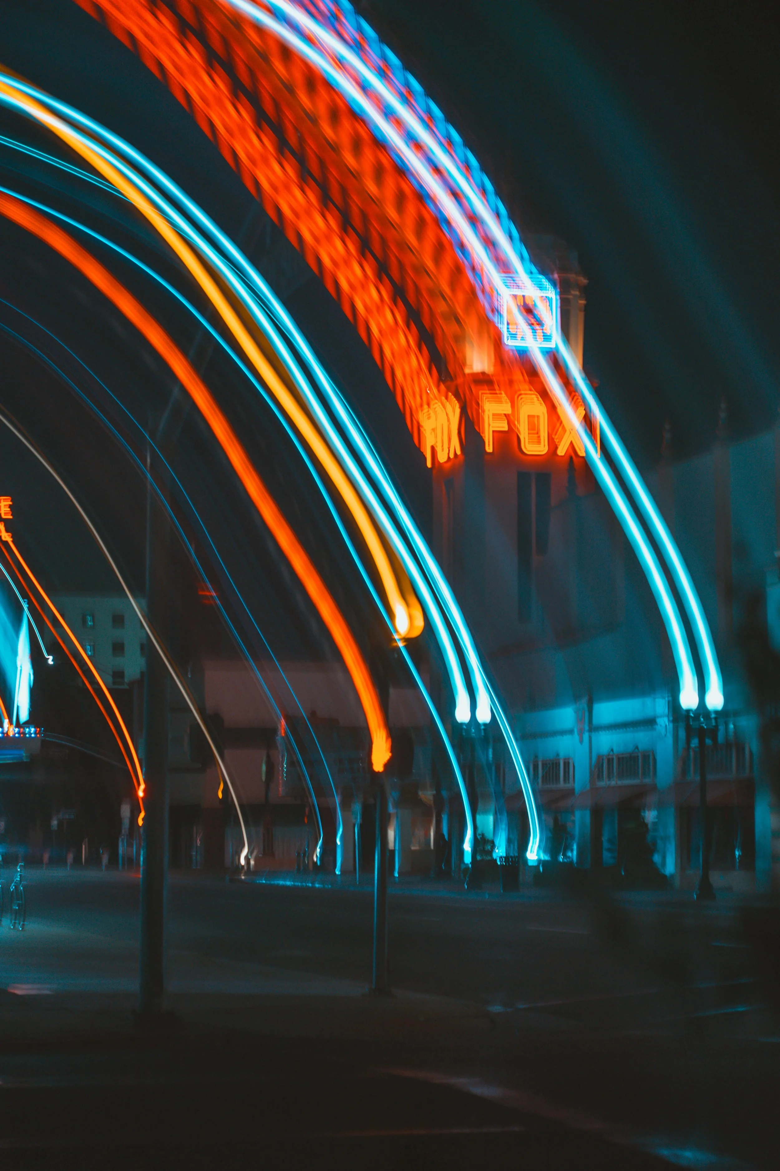 Nighttime scene of a neon-lit Ferris wheel with blue, orange, and red lights, and a illuminated sign reading "Fox" in the background.