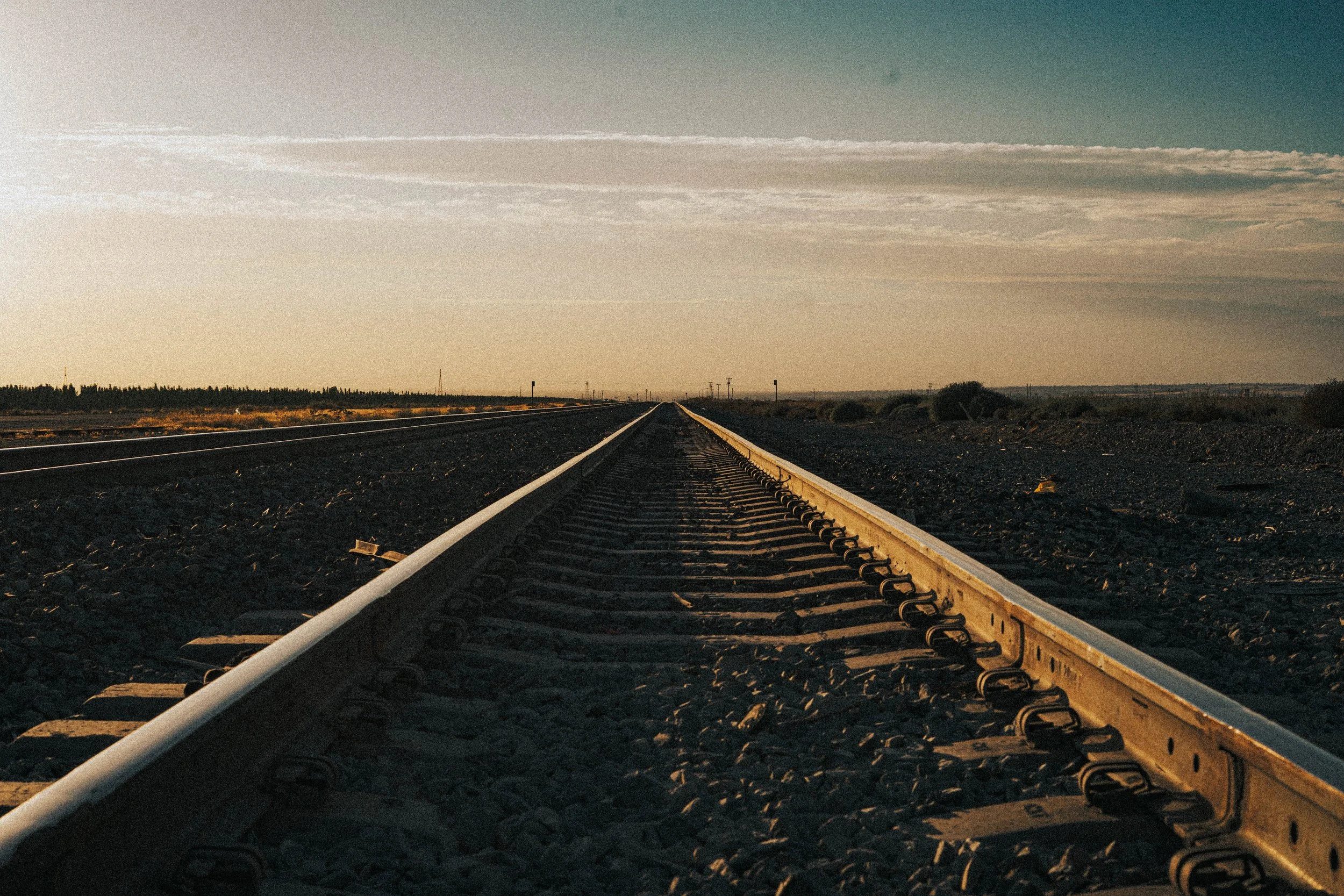 A straight view of railroad tracks extending into the horizon during sunset.