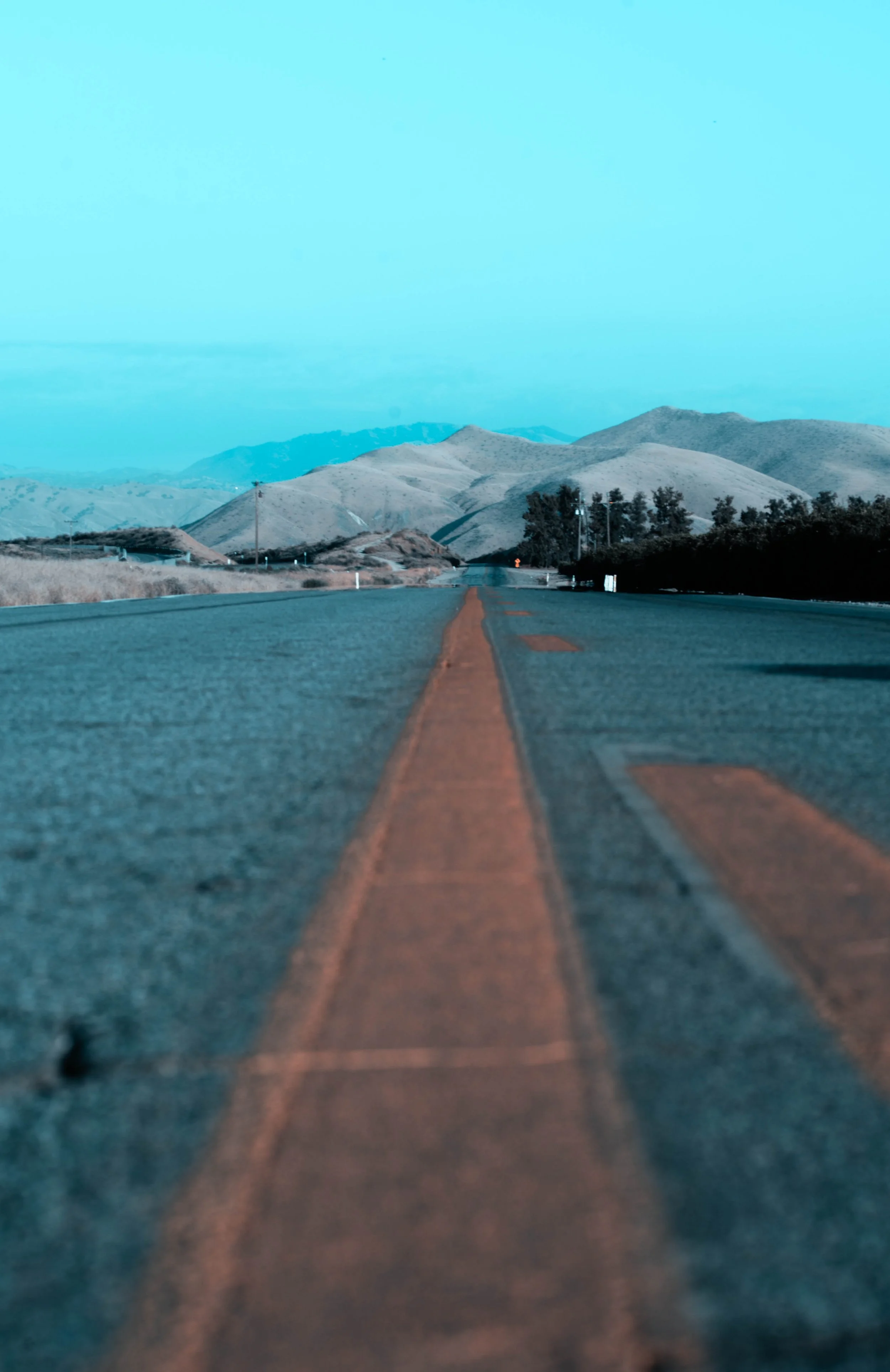 A straight road leading towards mountains in the distance under a blue sky.