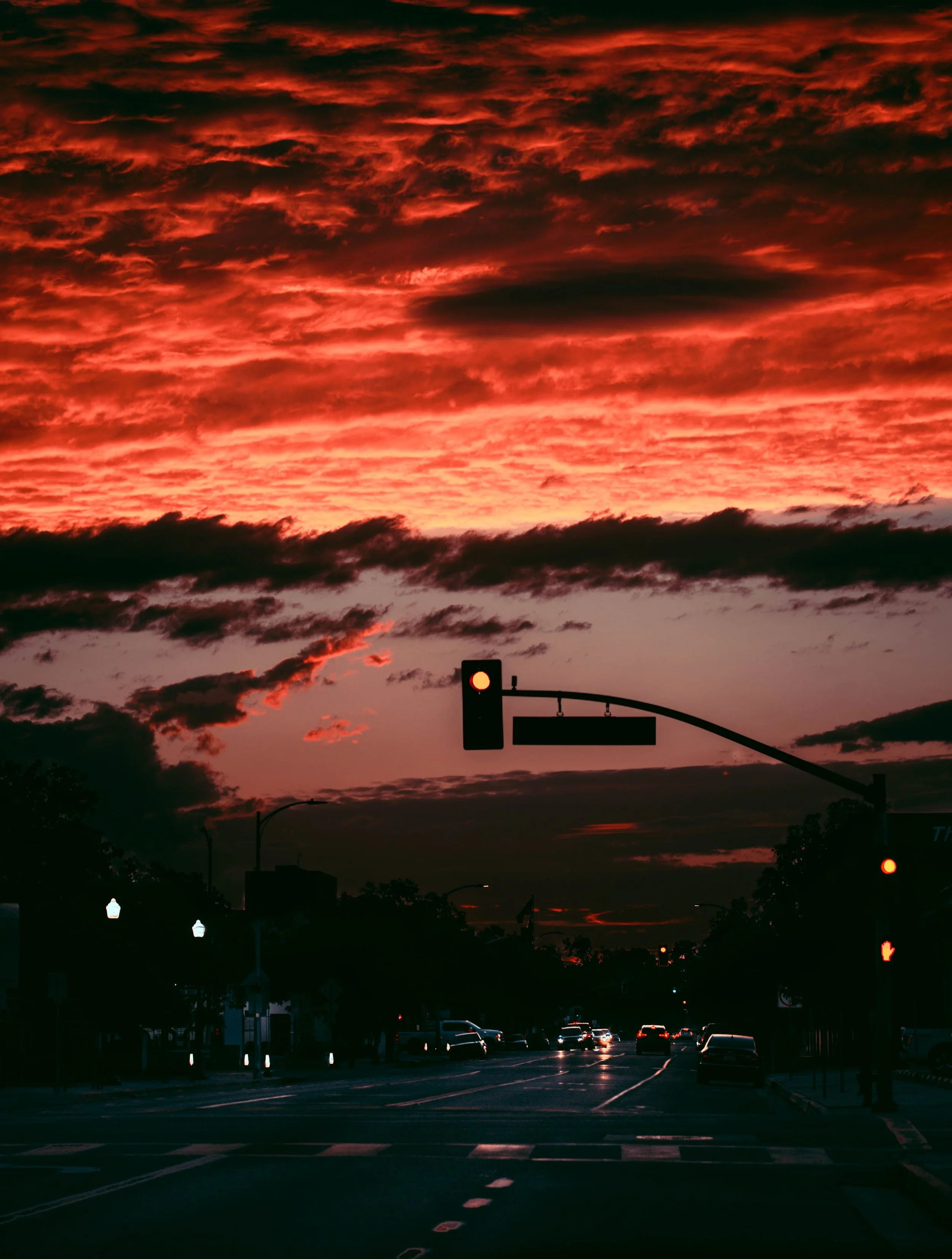 A traffic light at a city intersection during a dramatic, cloudy sunset with vibrant red and orange skies.