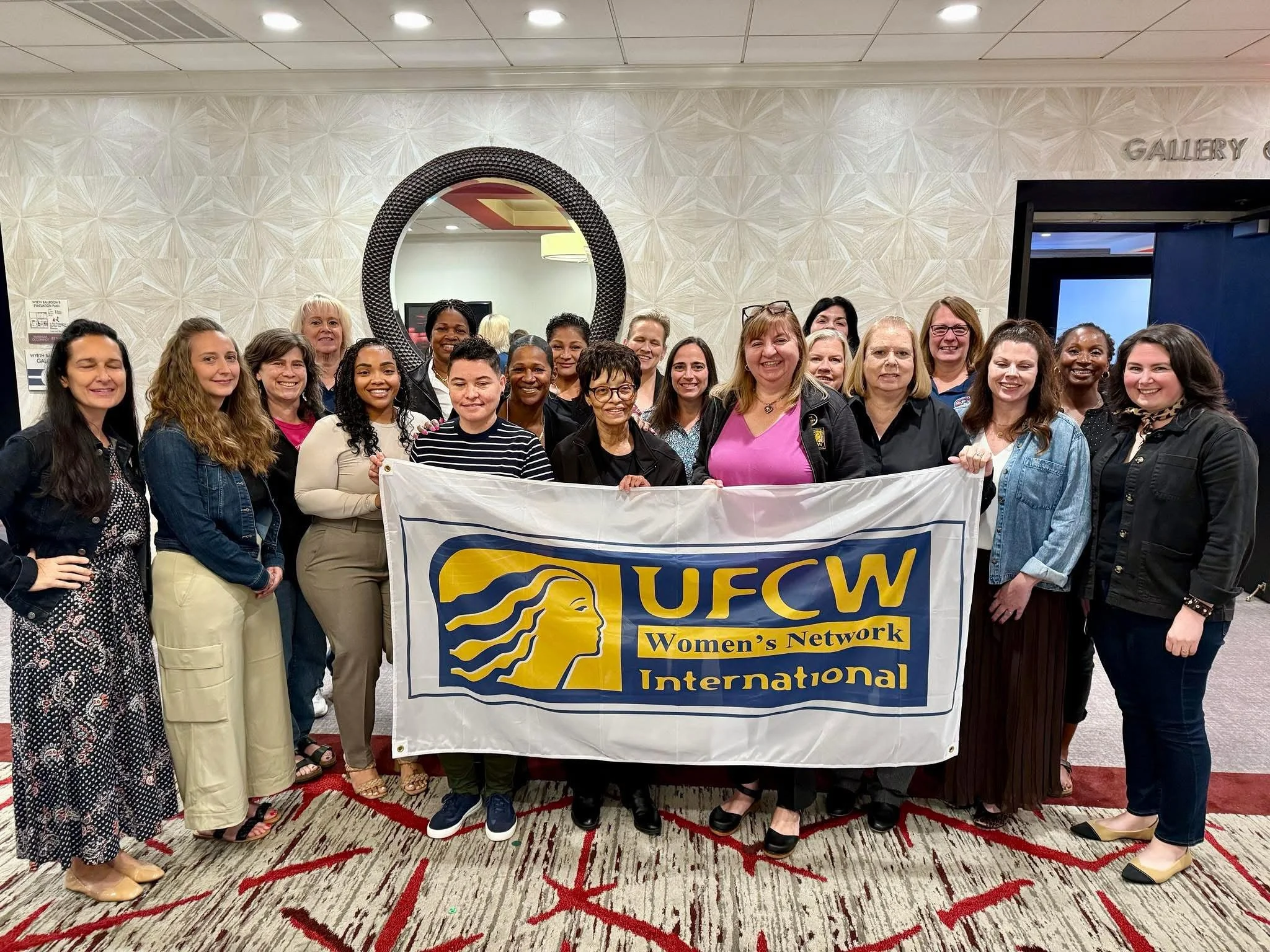 Group of women and girls holding a banner for UFCW Women's Network International, standing in a hotel conference room.