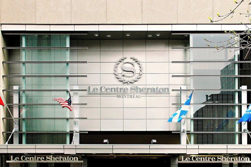 Exterior view of the Le Centre Sheraton hotel in Montreal, featuring the hotel name on the facade and several flags, including the American and Quebec flags.