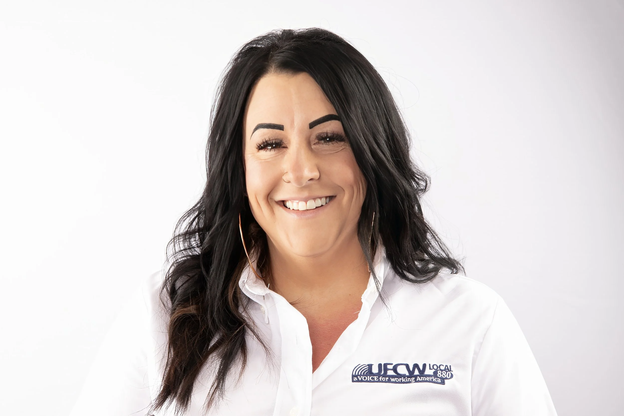 A smiling woman with dark hair wearing a white shirt with the UFCW Local 880 logo.