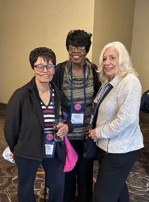 Three women smiling at a conference, wearing name badges, standing on patterned carpet.