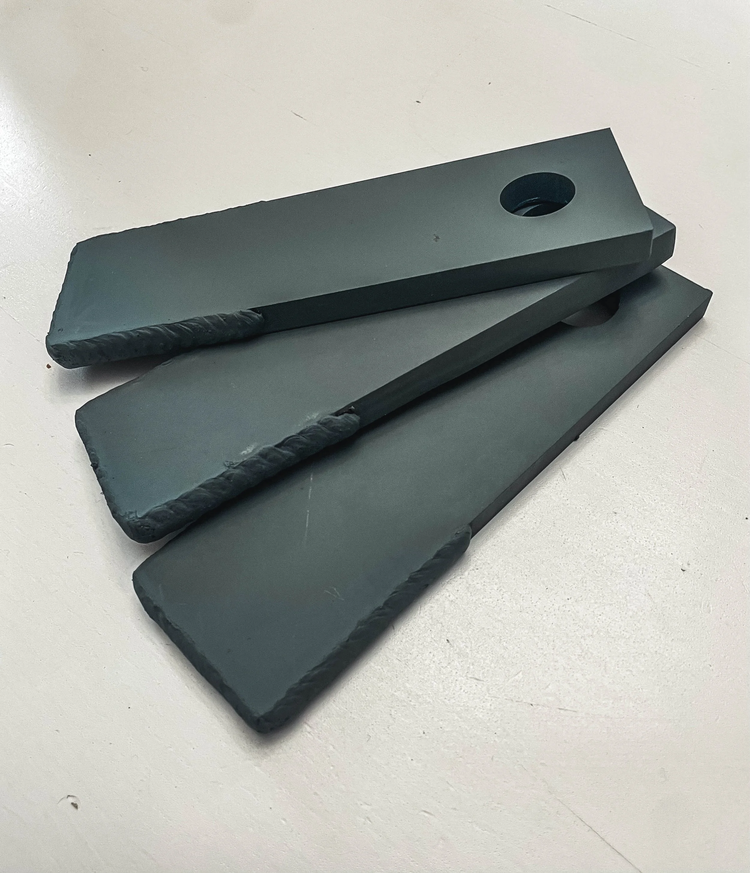 Three black sharpening stones stacked on a white surface, with the top stone having a hole for a finger grip.