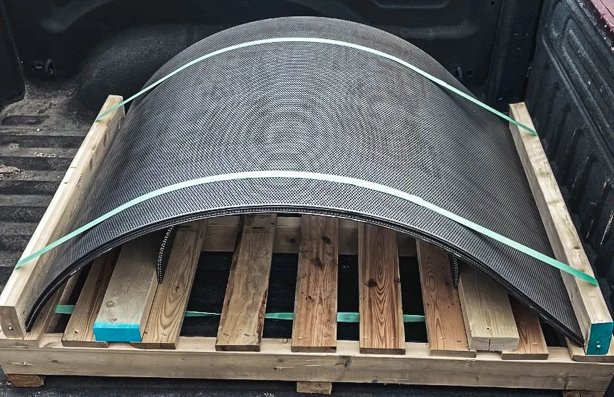 A carbon fiber car fender on a wooden pallet secured with green straps.