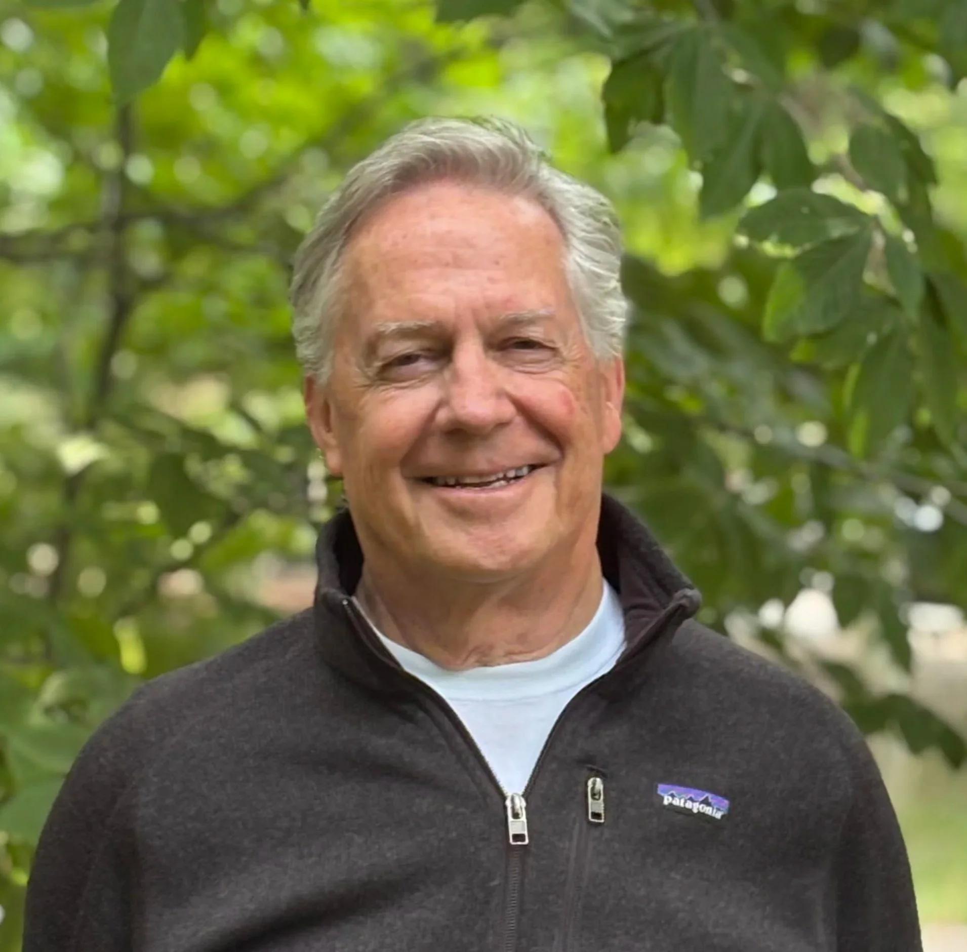 Close-up of Michael Griffin wearing a black Patagonia fleece jacket, outdoors with green leaves in the background.