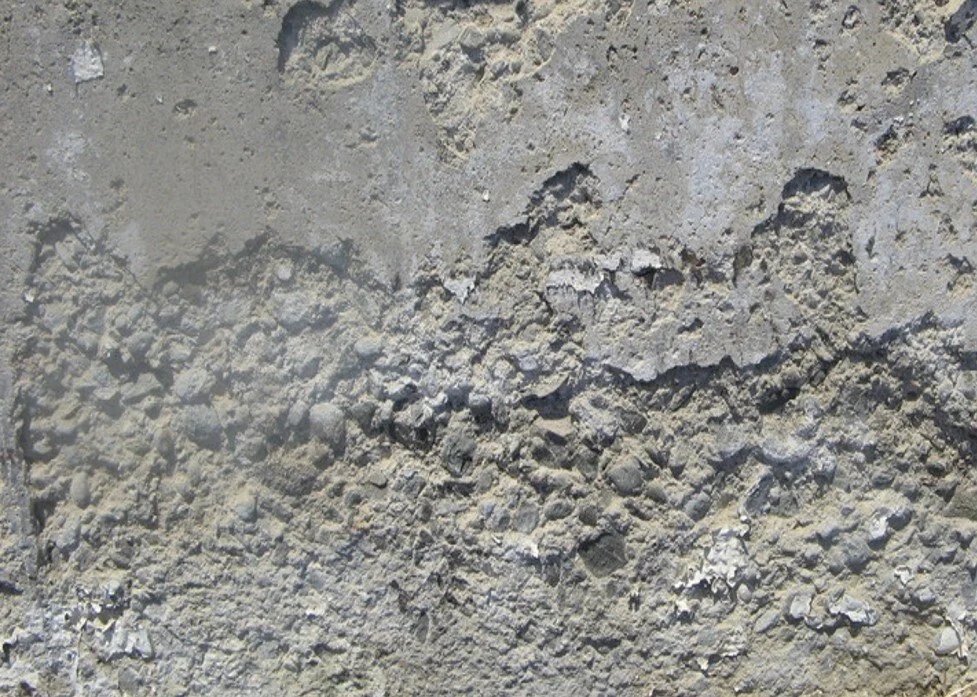Close-up of rough, textured gray concrete surface with small pebbles and cracks.