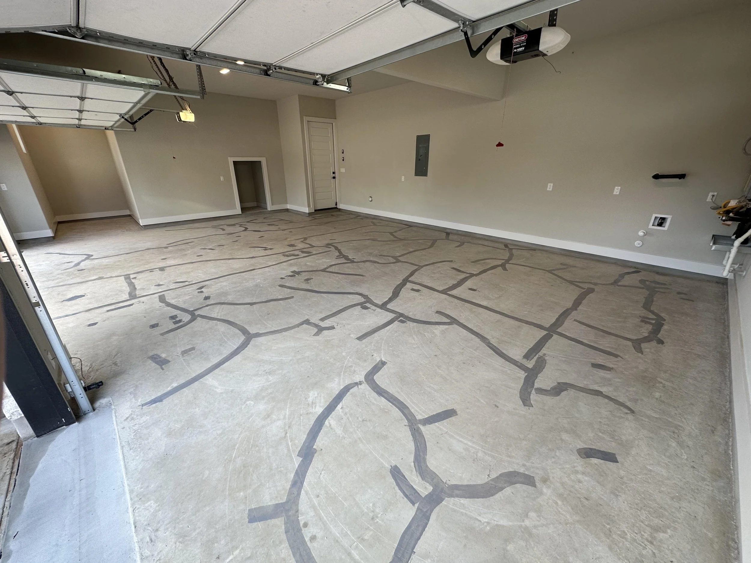 Empty garage with cracked concrete floor marked with dark tape lines, white walls, garage door openers, and a door leading to the interior of the house.