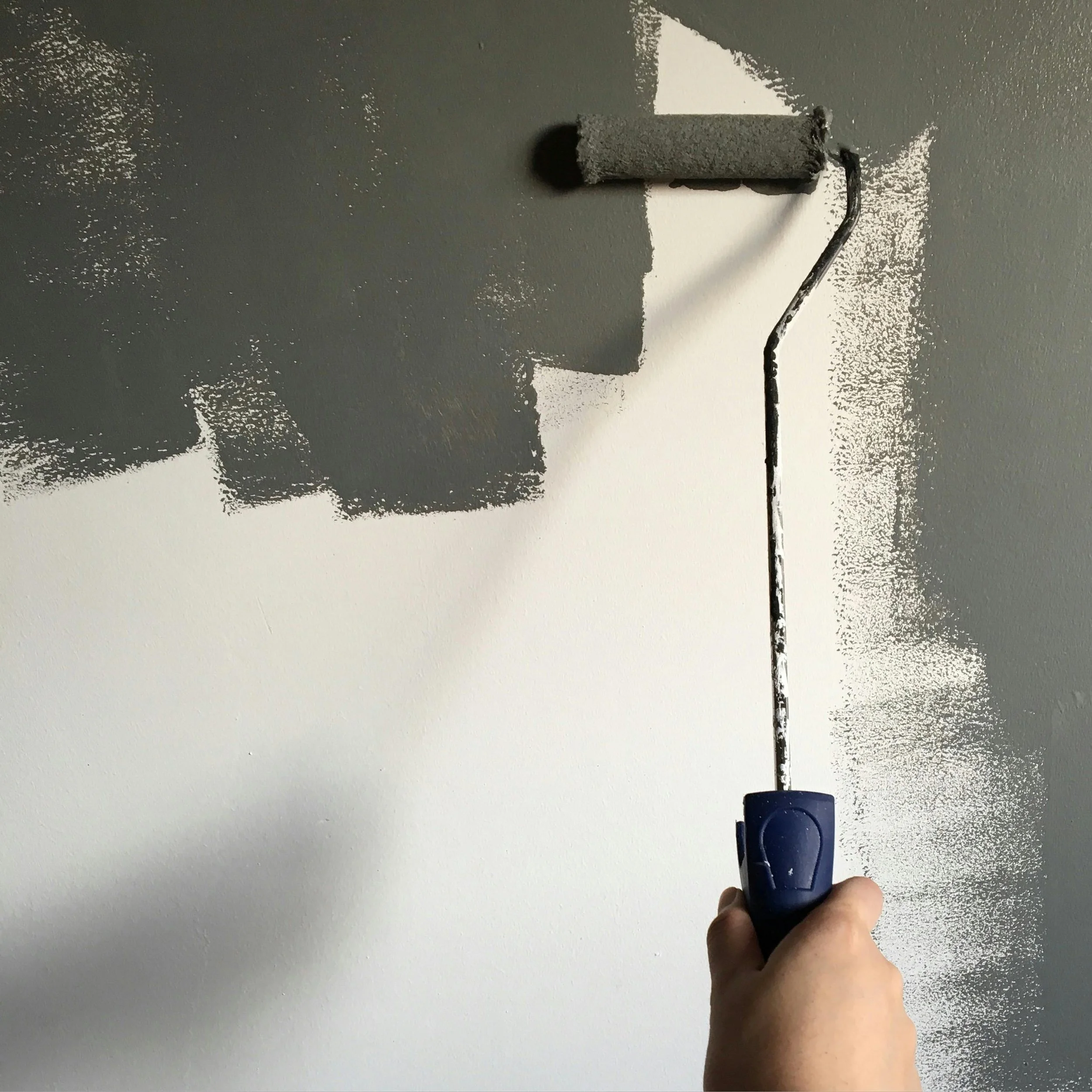 Person painting a ceiling with a paint roller on an extendable handle.