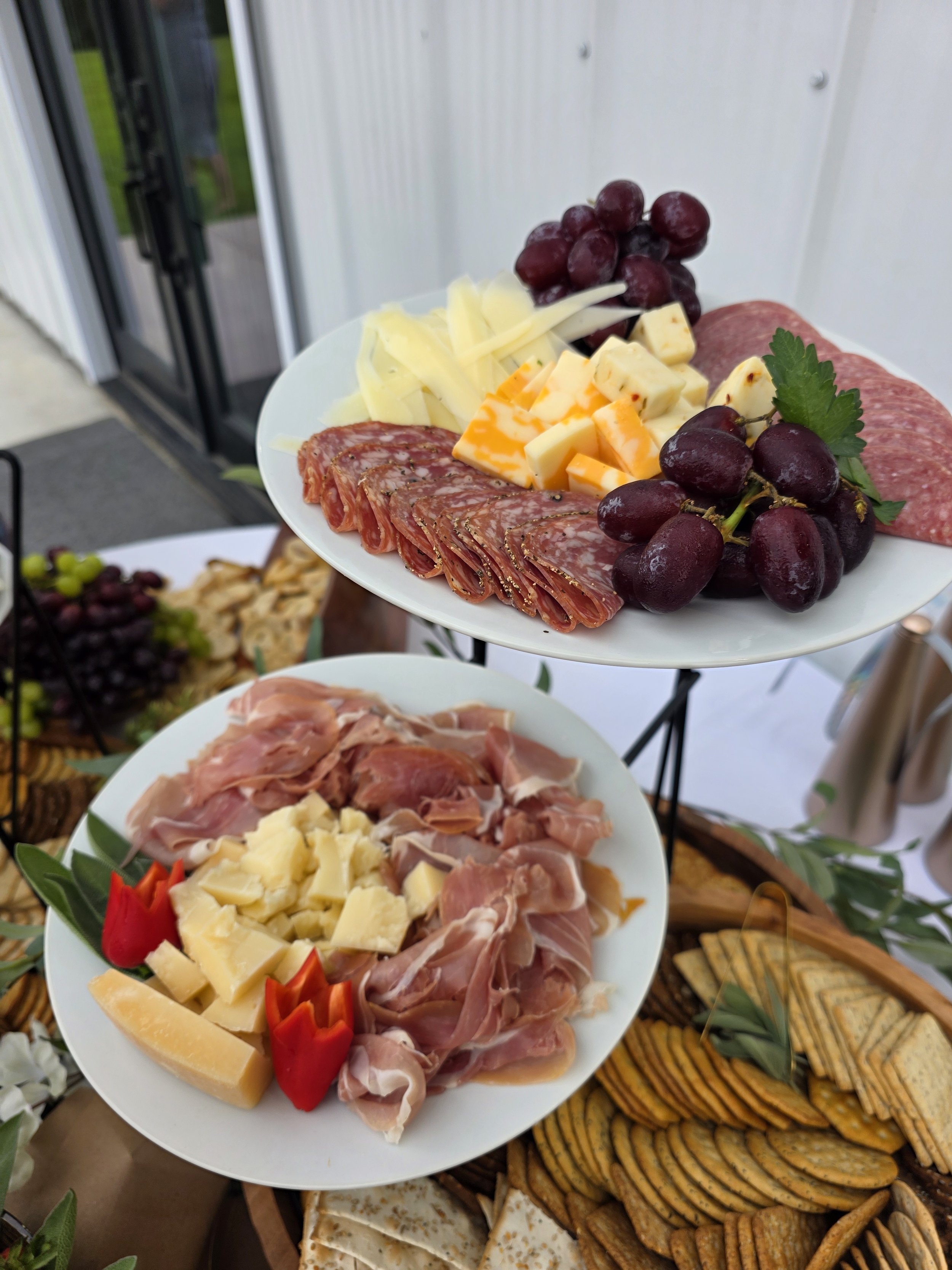 Charcuterie platter with various cheeses, grapes, and cured meats on a two-tiered serving tray.