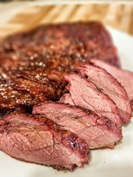 Sliced cooked steak on a white plate with a wooden cutting board in the background.