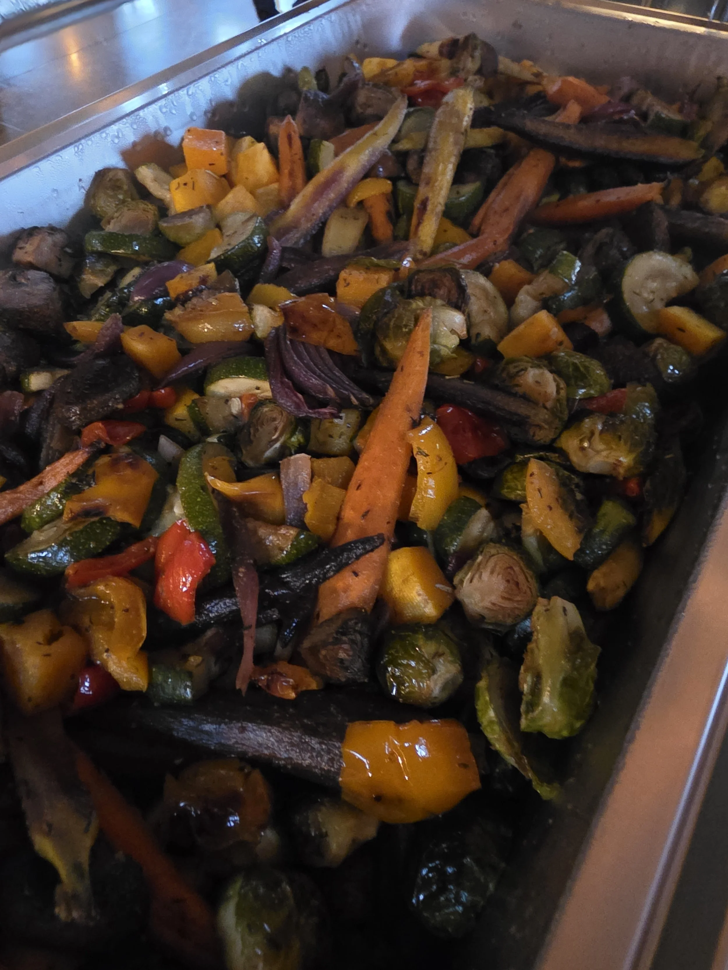 Roasted mixed vegetables including zucchini, yellow squash, red and orange bell peppers, carrots, red onions, and mushrooms in a baking tray.