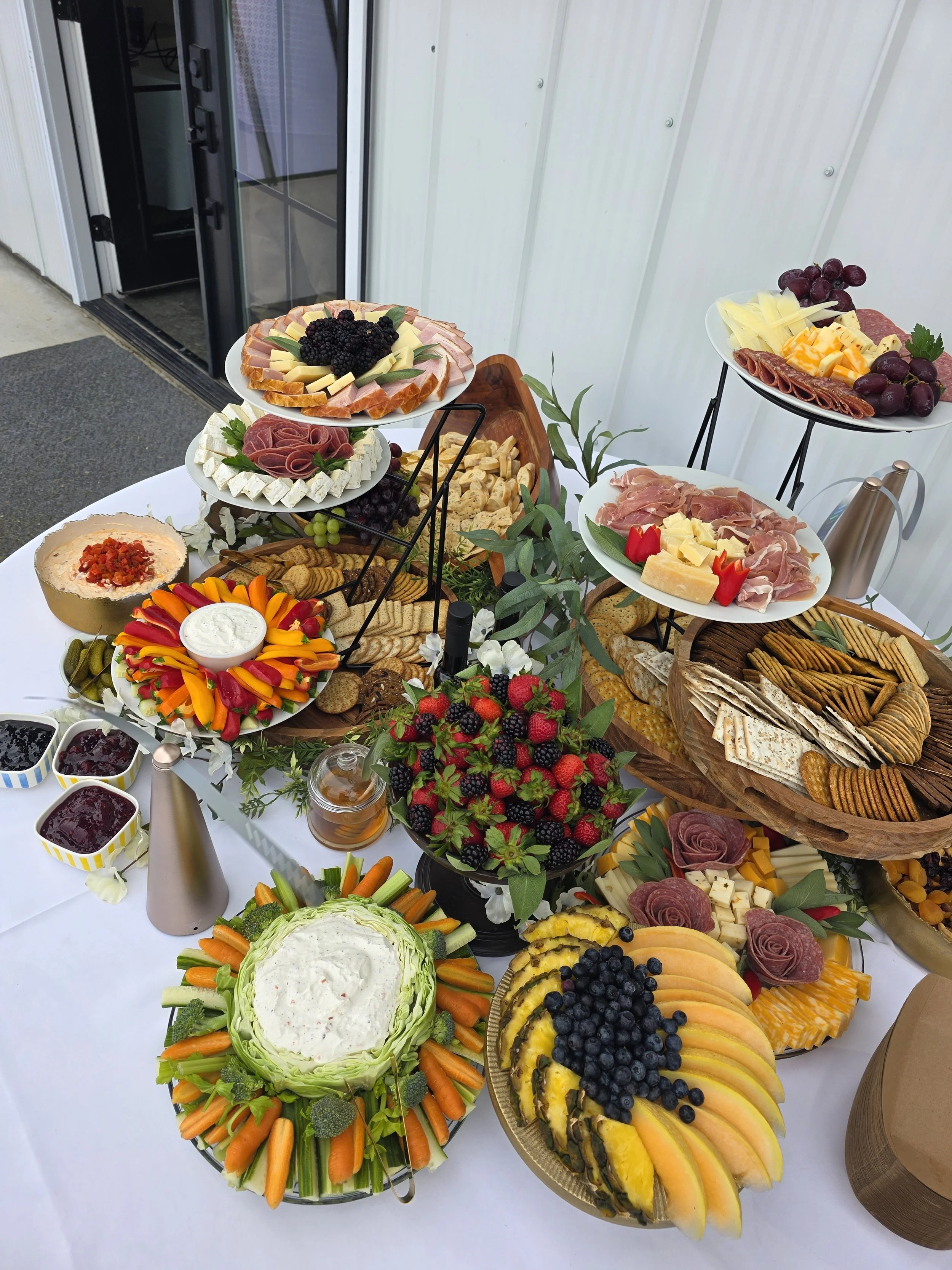 A buffet table with a variety of cheese, meat, fruit, vegetables, crackers, and condiments arranged on plates and bowls.