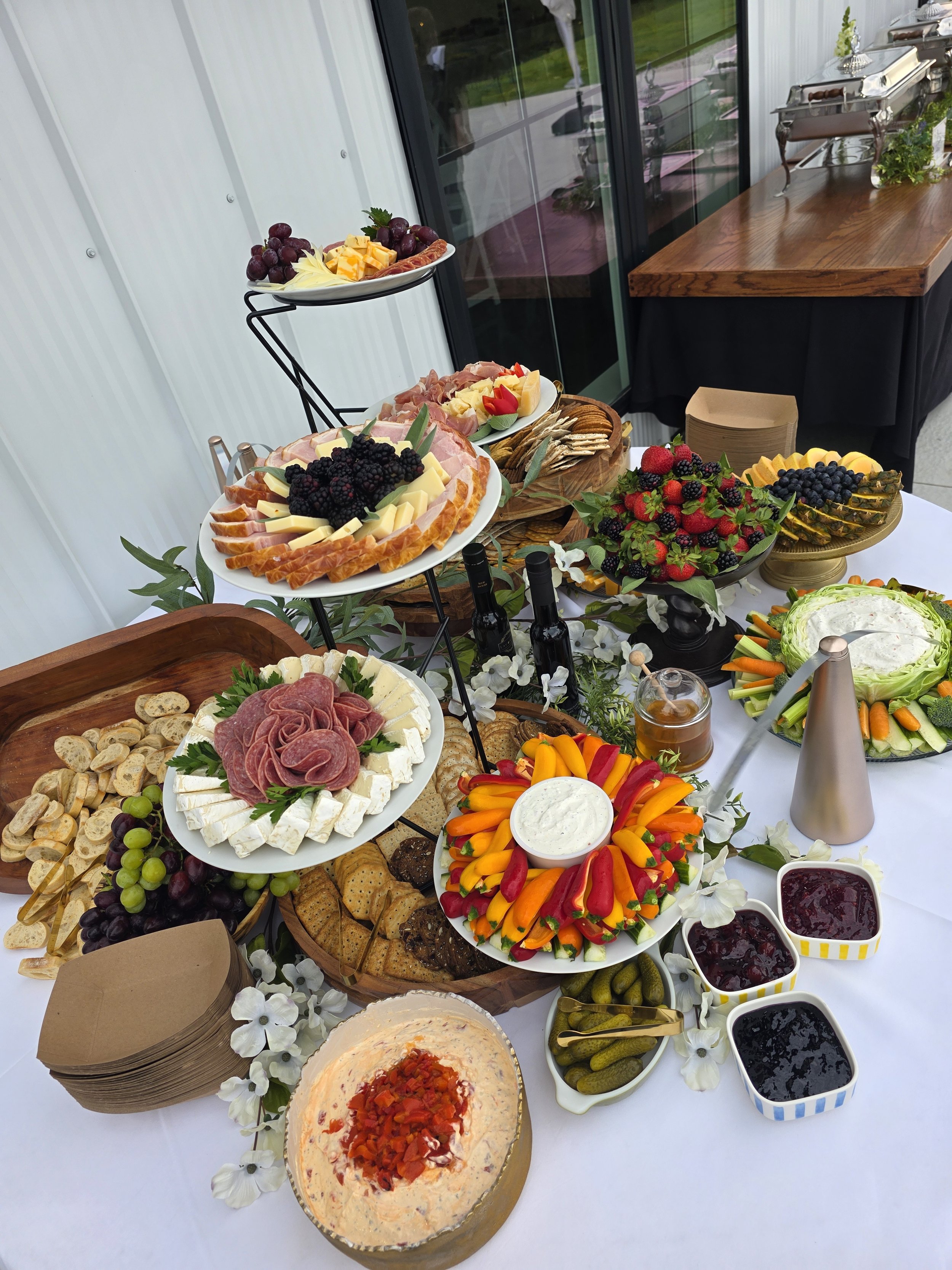 A table with a variety of appetizers and fruits, including cheese, meats, crackers, grapes, strawberries, blackberries, and a vegetable platter with dip, arranged for a gathering or celebration.