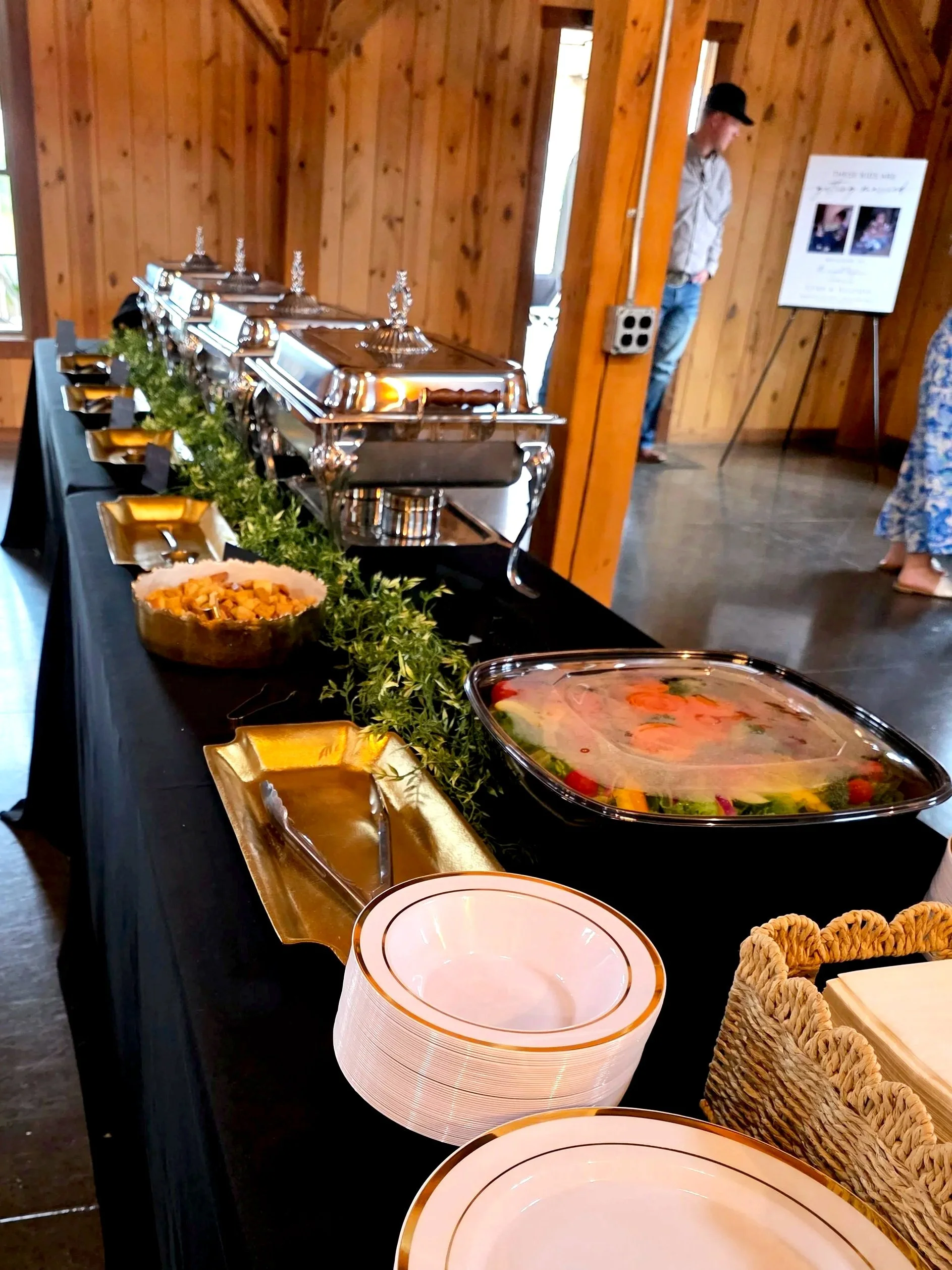 Buffet table with chafing dishes, a bowl of food, and empty plates in a wooden room.