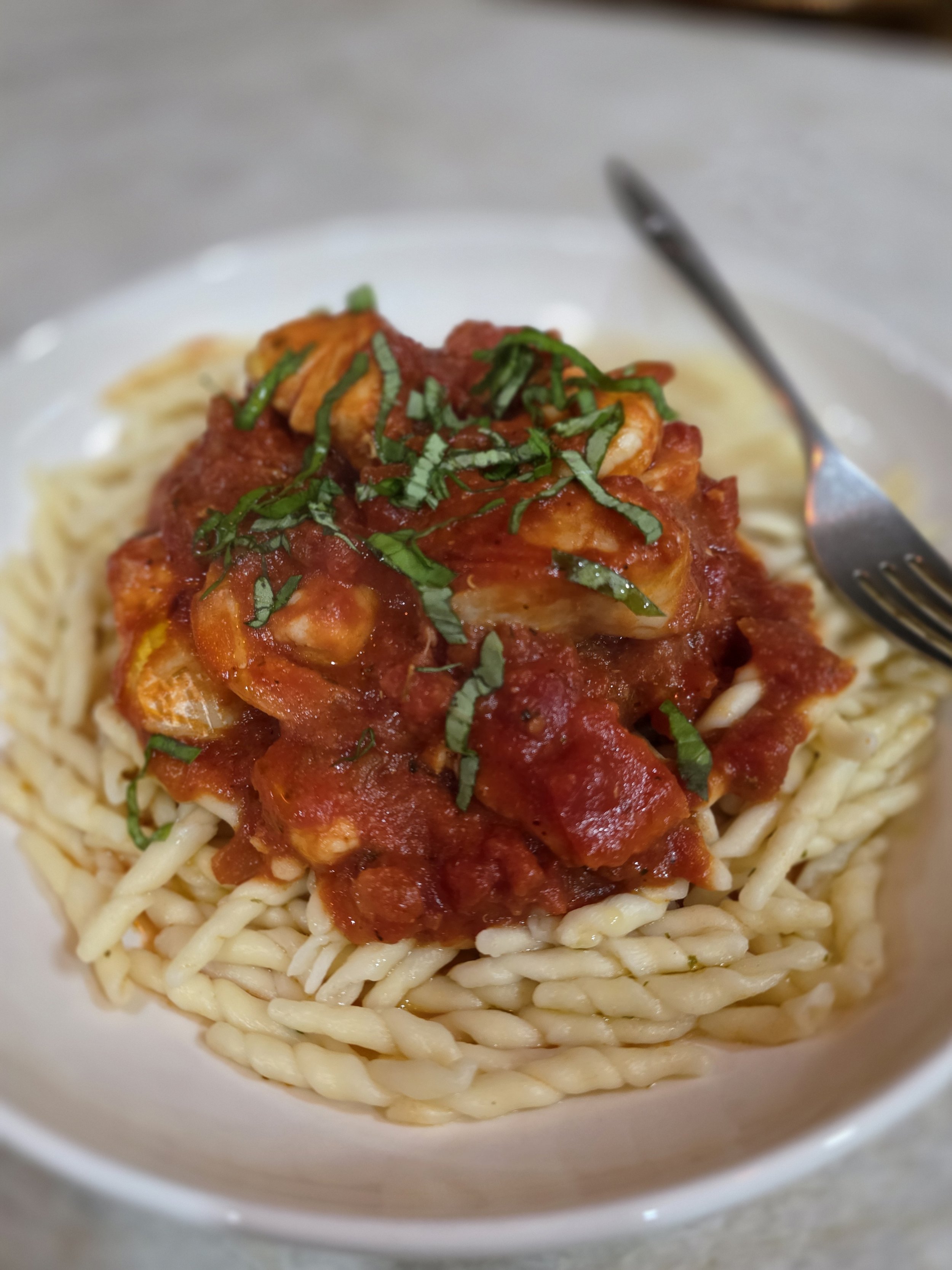 Close-up of a bowl of spaghetti topped with tomato sauce, pieces of chicken, chopped herbs, and served on a white plate.