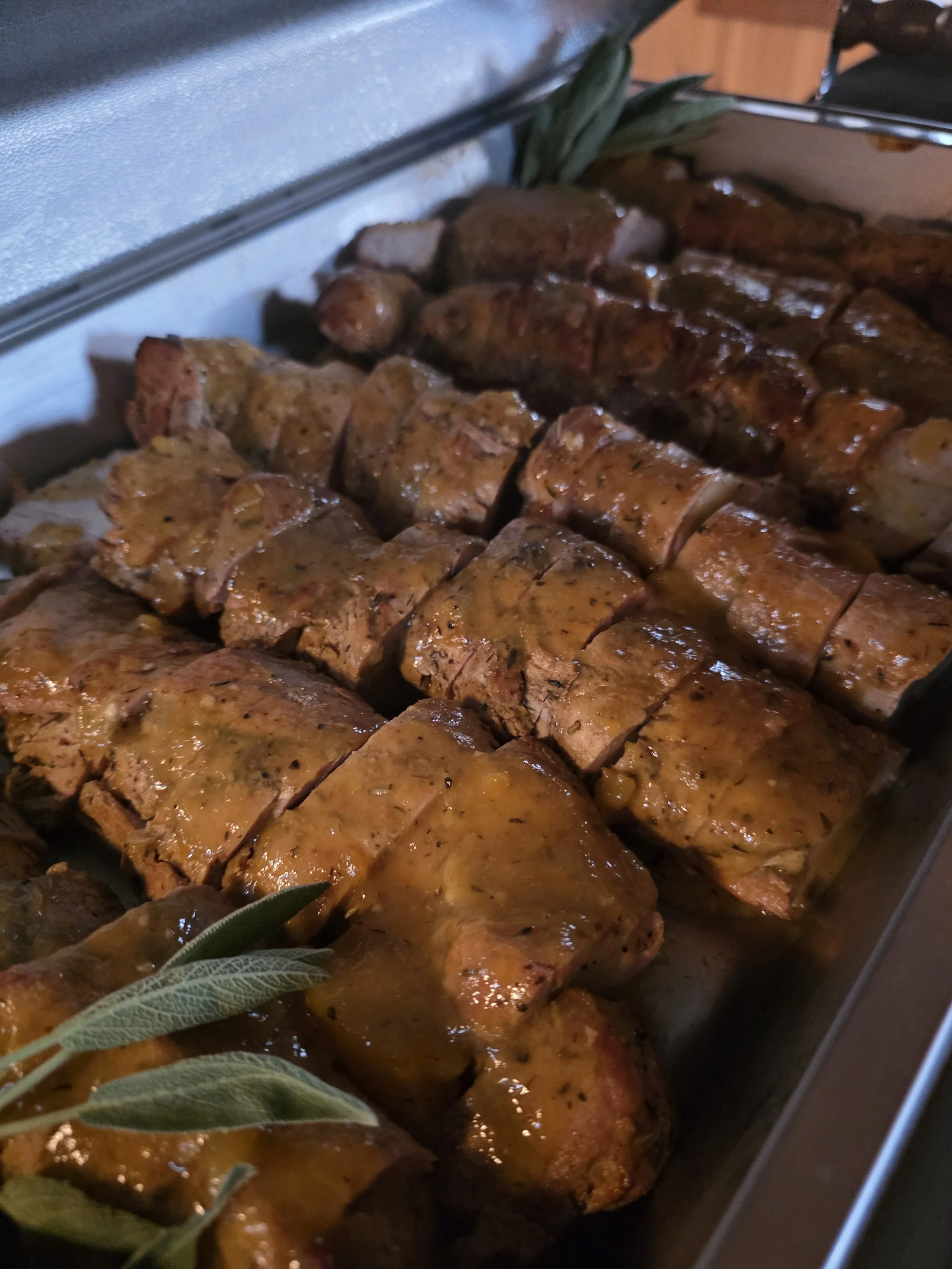 Close-up of pork tenderloin with peach glaze slices on a serving tray garnished with fresh herbs.