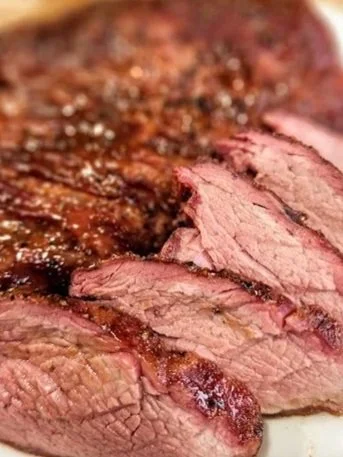 Close-up of a cooked steak, sliced to reveal a pink interior, with a browned crust on the outside.