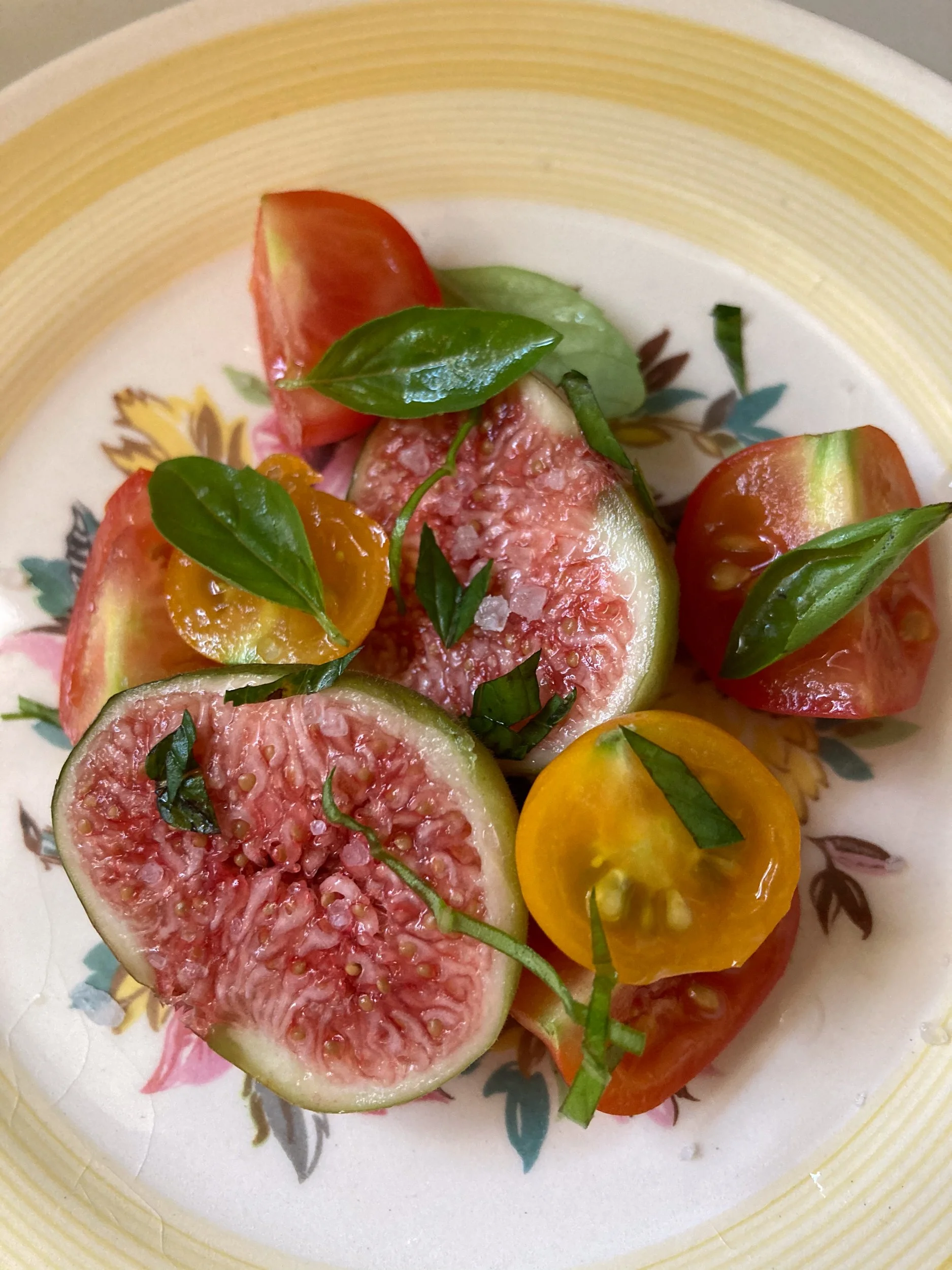 Sliced heirloom tomatoes with basil leaves on a decorative plate.