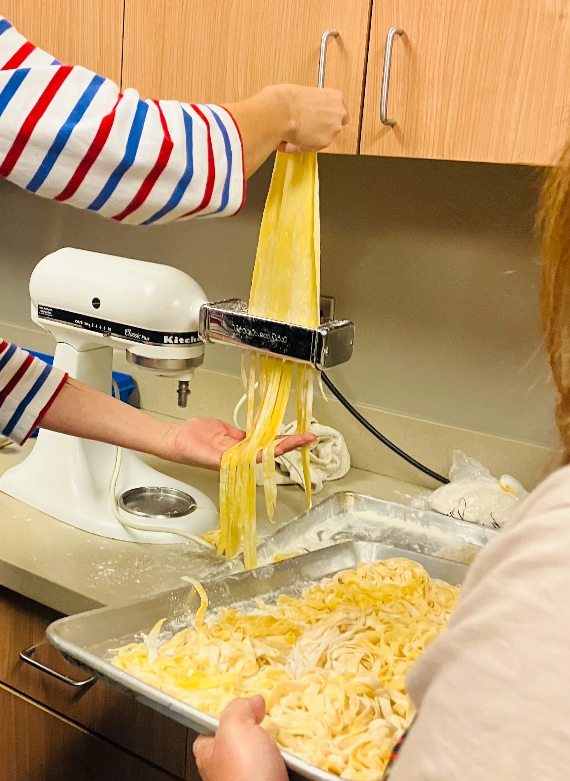 Person holding homemade pasta with a pasta machine in a kitchen