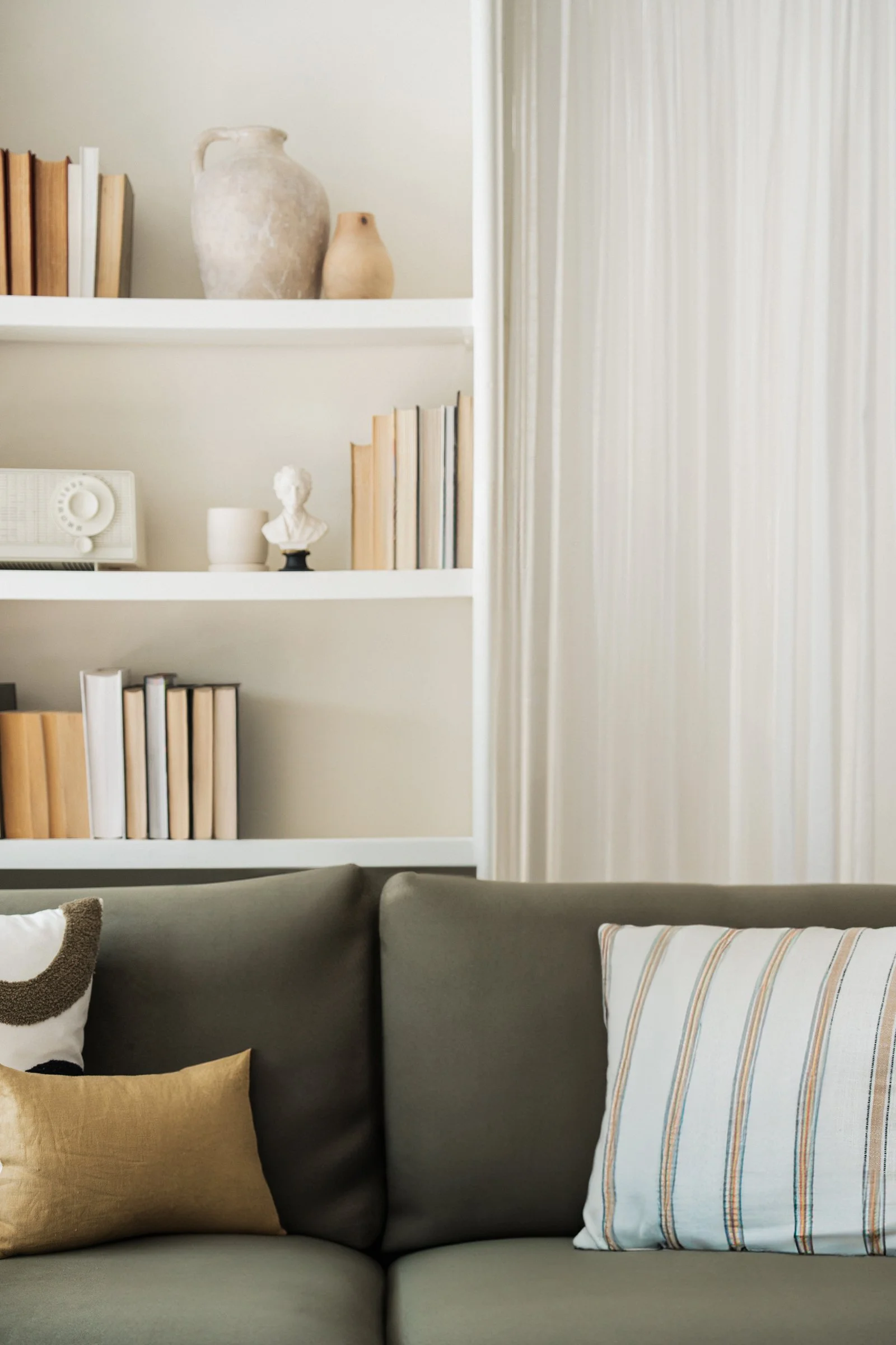 A living room with bookshelves, decorative objects, a radio, sculptures, and pillows on a sofa.