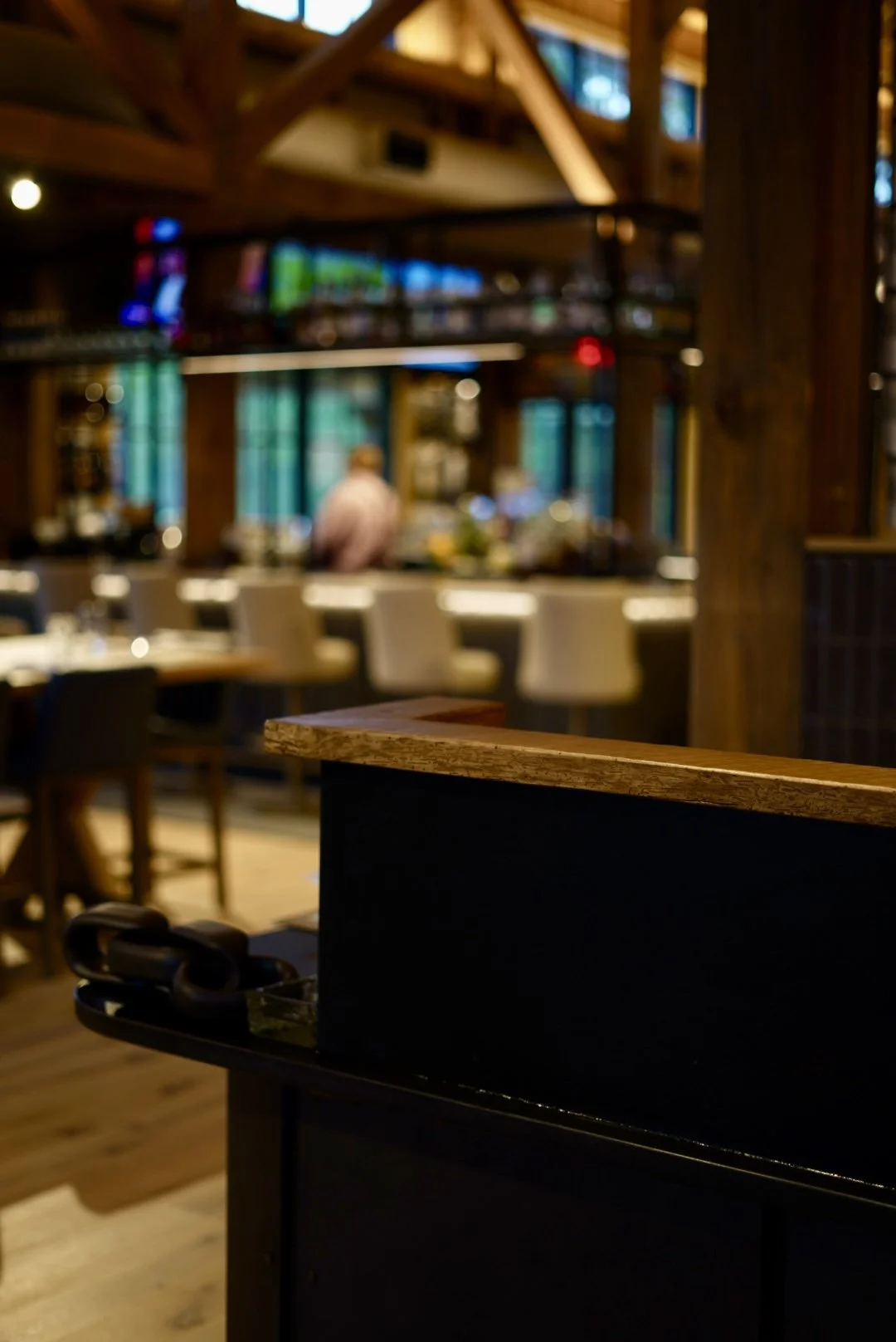 Blurred interior of a warmly lit restaurant or bar with tables, chairs, colorful lights, and a wooden counter in the foreground.